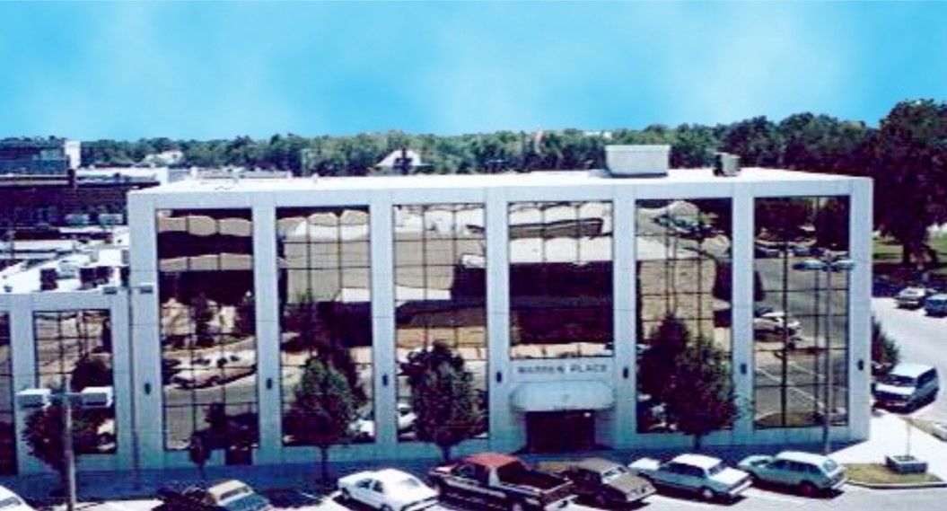 Exterior view of the Museum of Art building; modern white with large windows. Cars and trees are in front.