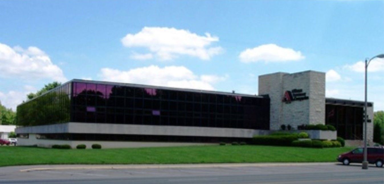 Office building with dark glass windows, a light-colored stone facade, and a well-manicured lawn. Blue sky.