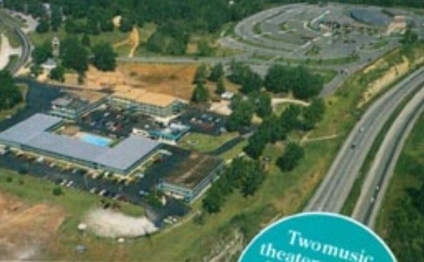 Aerial view of a hotel complex with a swimming pool, parking, and a highway running alongside.
