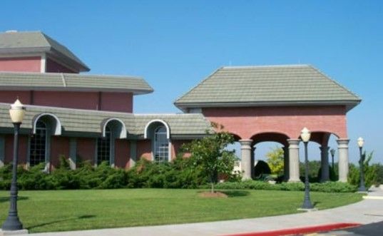 Building with red exterior and gray tiled roofs; arched entryway with columns; blue sky.