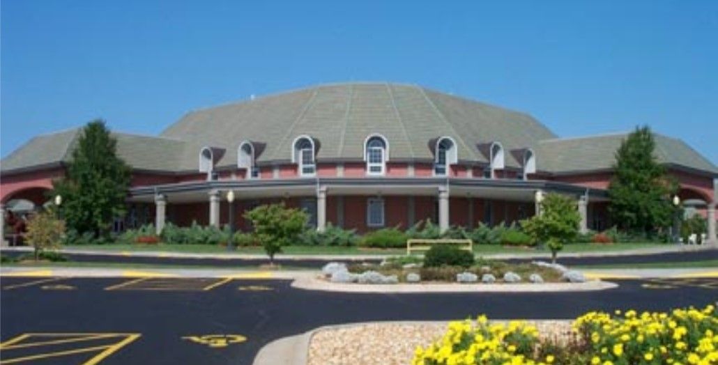 Large, light-colored building with a domed roof and surrounding landscaping, blue sky overhead.