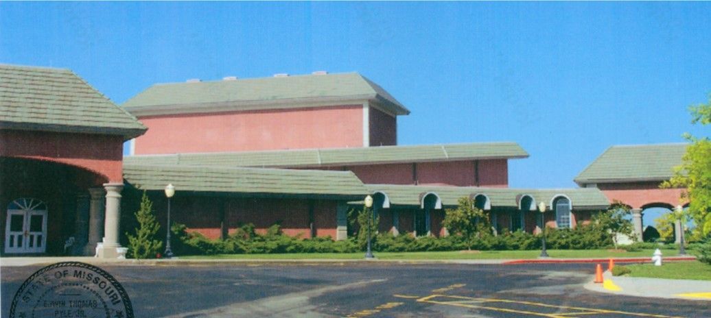 Red brick building with green roof, a blue sky in the background, and a paved road in the foreground.