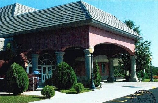 Building with a red brick exterior, arched entryway, and gray tile roof; green bushes in front.