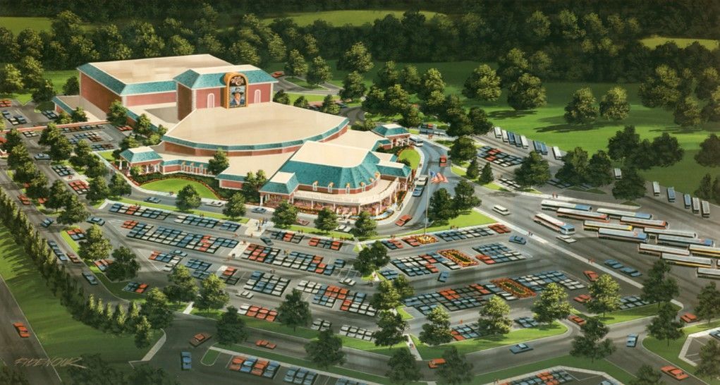 Aerial view of a large entertainment complex with parking lots filled with cars and surrounding trees.
