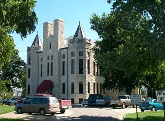 Stone building with turrets, arched windows, and parked vehicles.