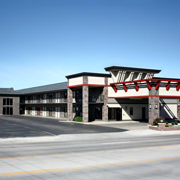 Hotel exterior with stone and red accents on a sunny day. Empty parking lot in front of the building.