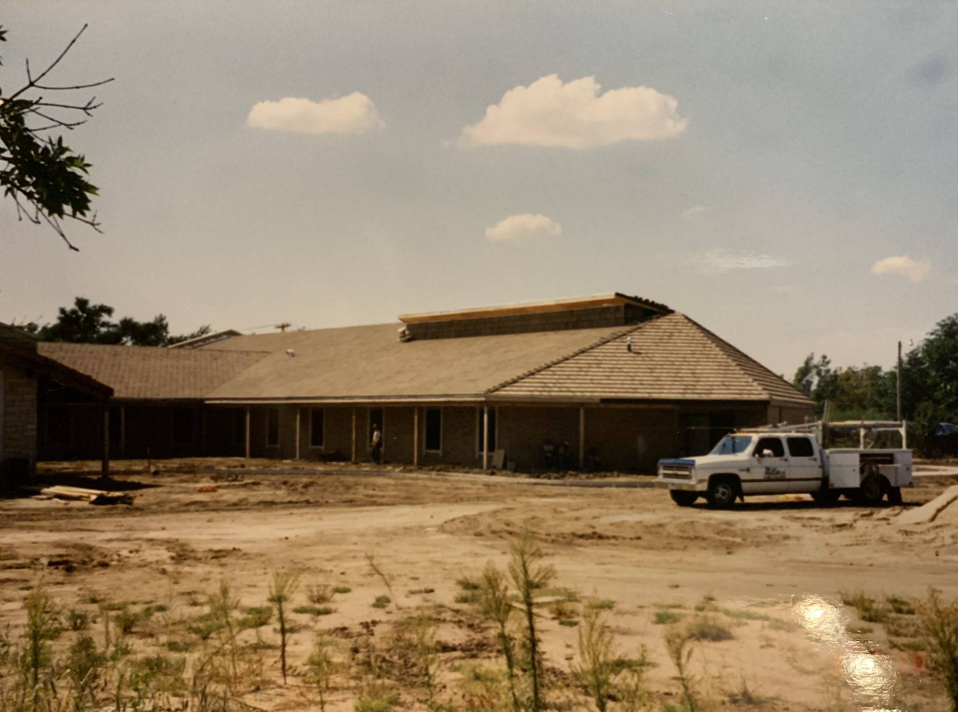 Building under construction with a white pickup truck on a dirt lot under a cloudy sky.