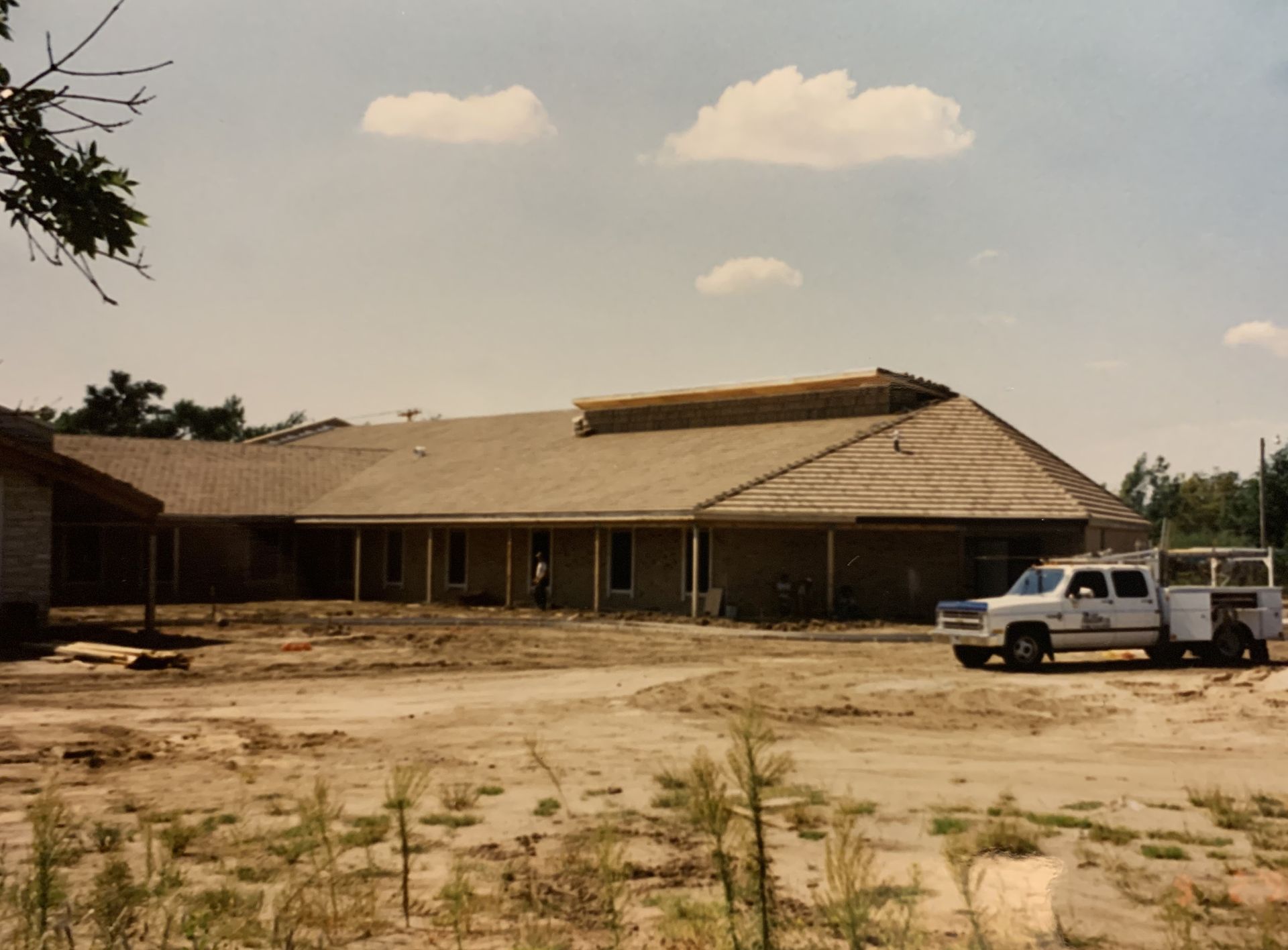 Building under construction, light-colored brick exterior, truck parked nearby on dirt lot, sunny day.