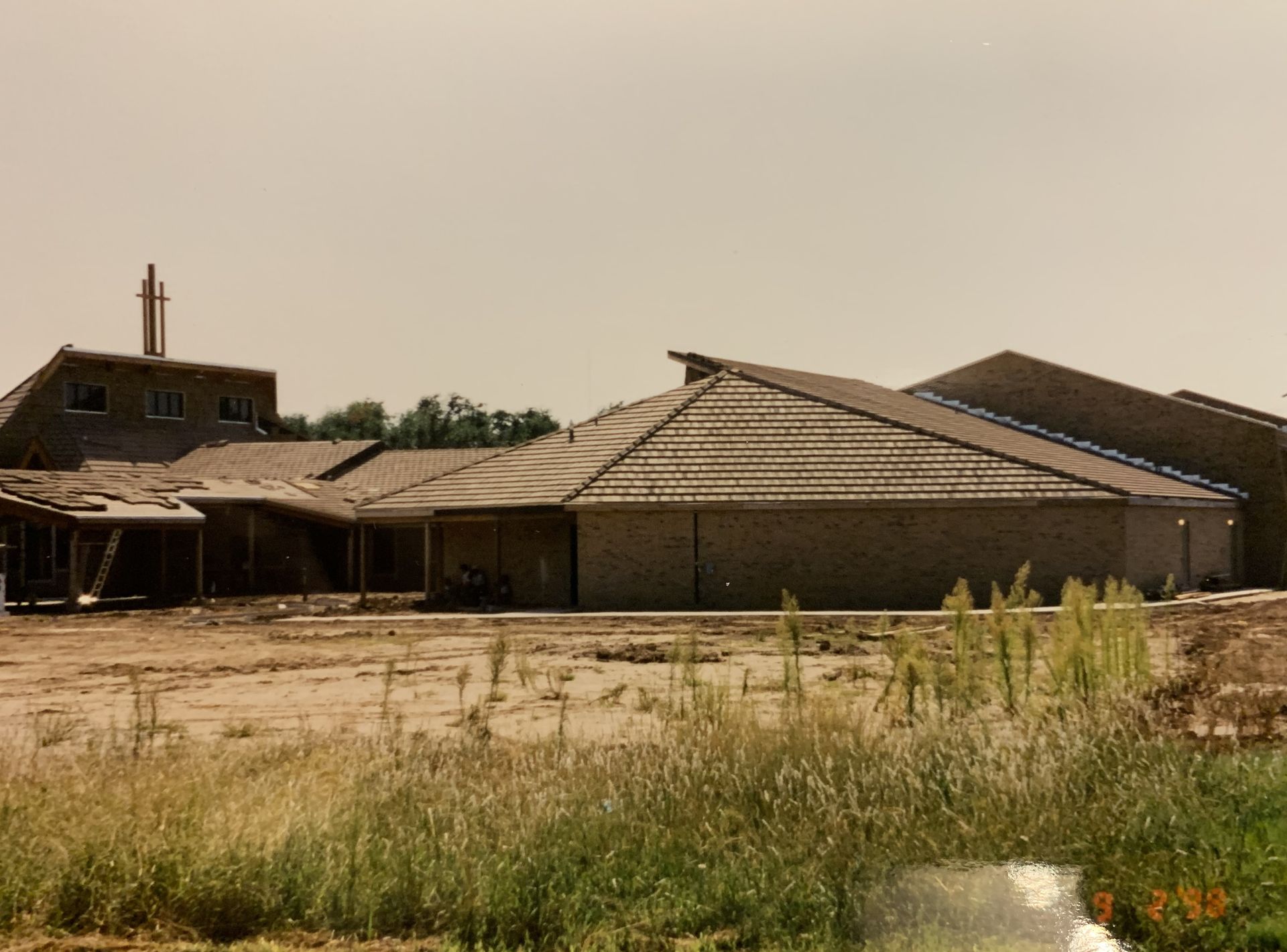 Building under construction with a brick exterior and a brown roof, set in a dry, grassy field.