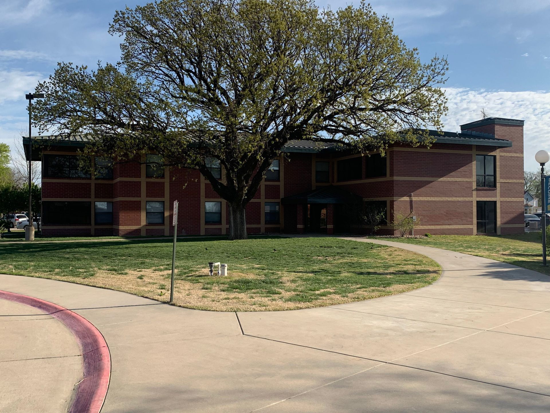 Brick building with large tree in front. Sidewalk leads to entrance.