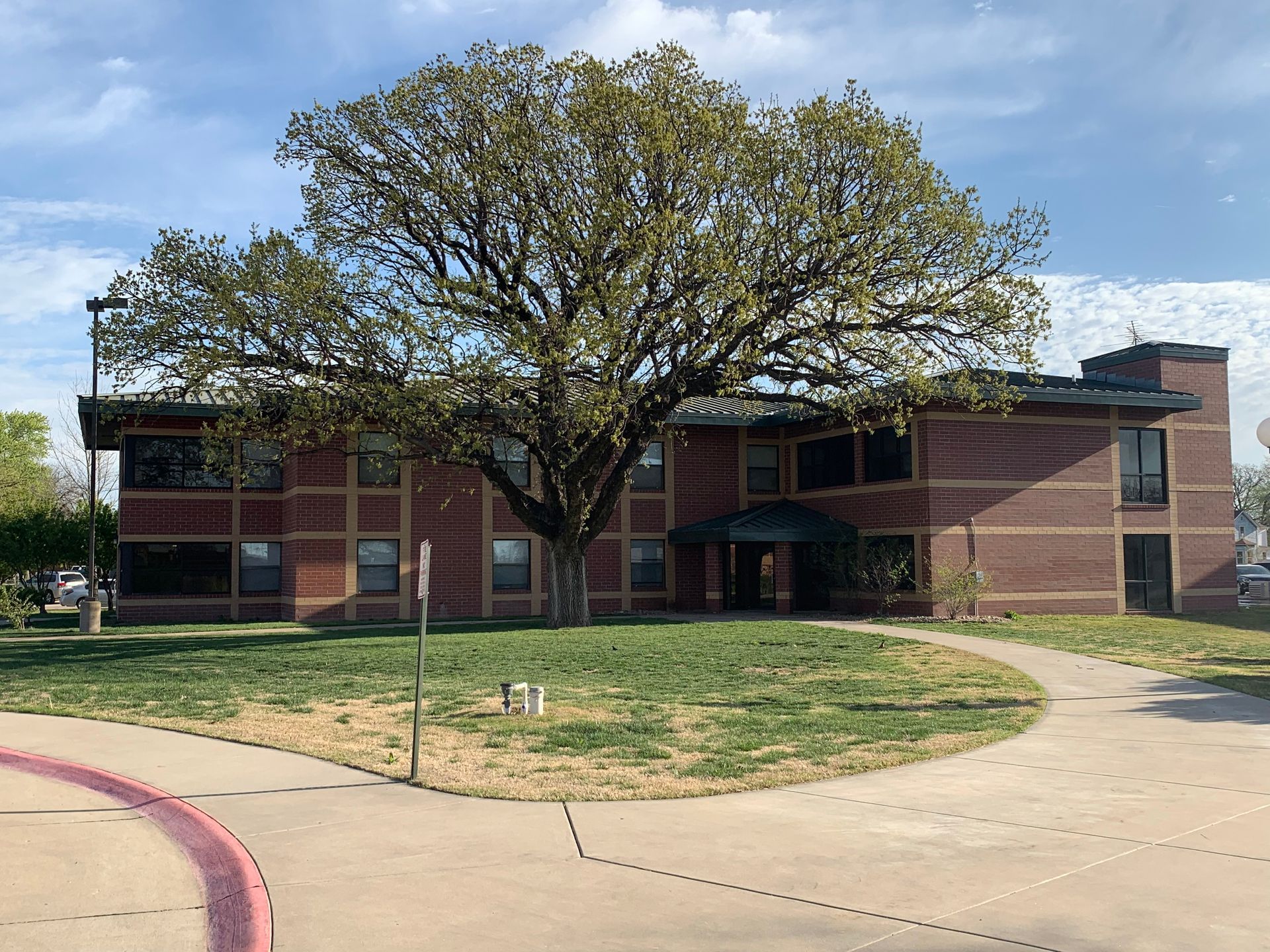Two-story brick building with a large tree in front; green lawn, walkway, overcast sky.
