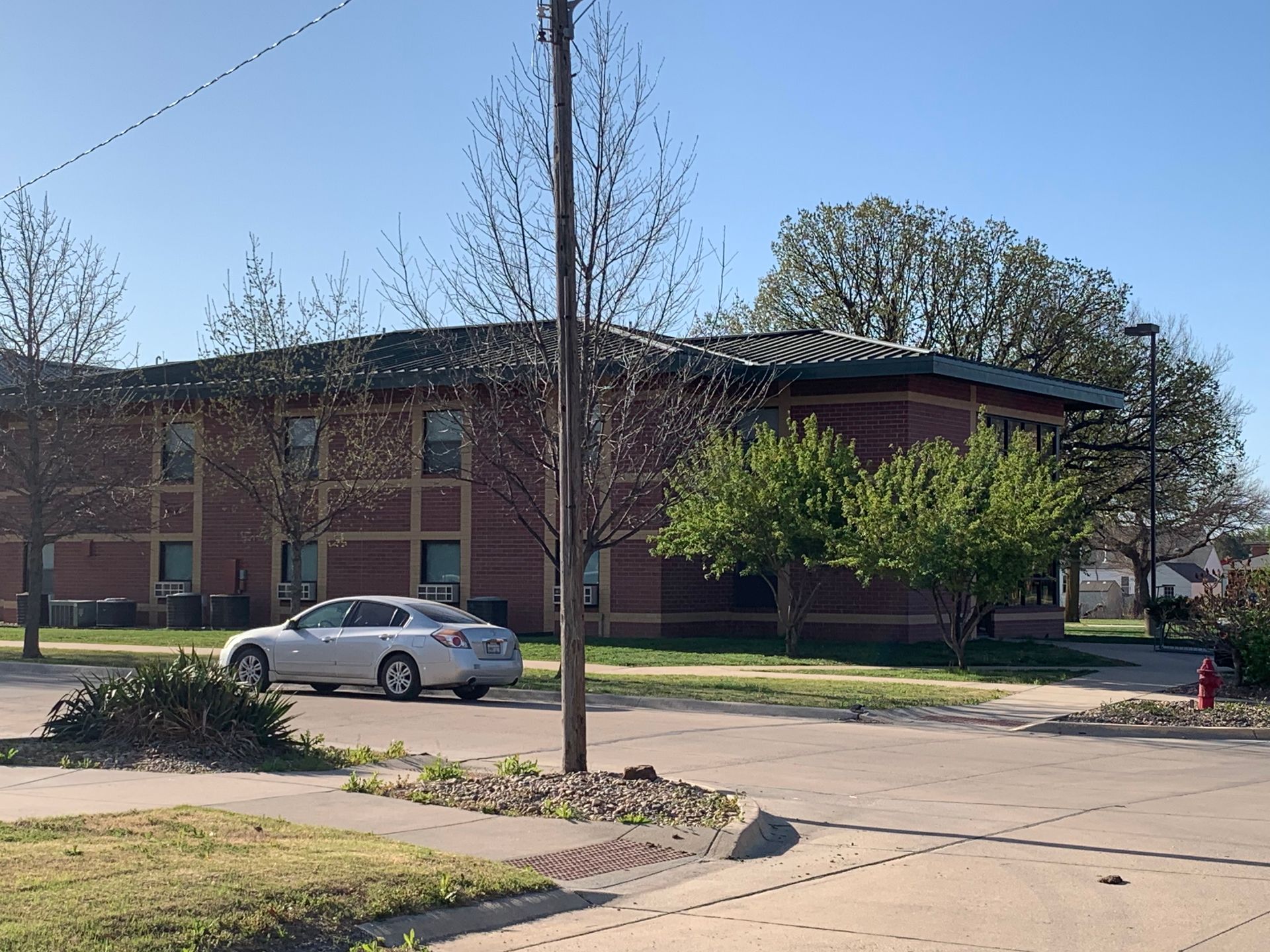 A silver car parked on a street in front of a brick building on a sunny day.