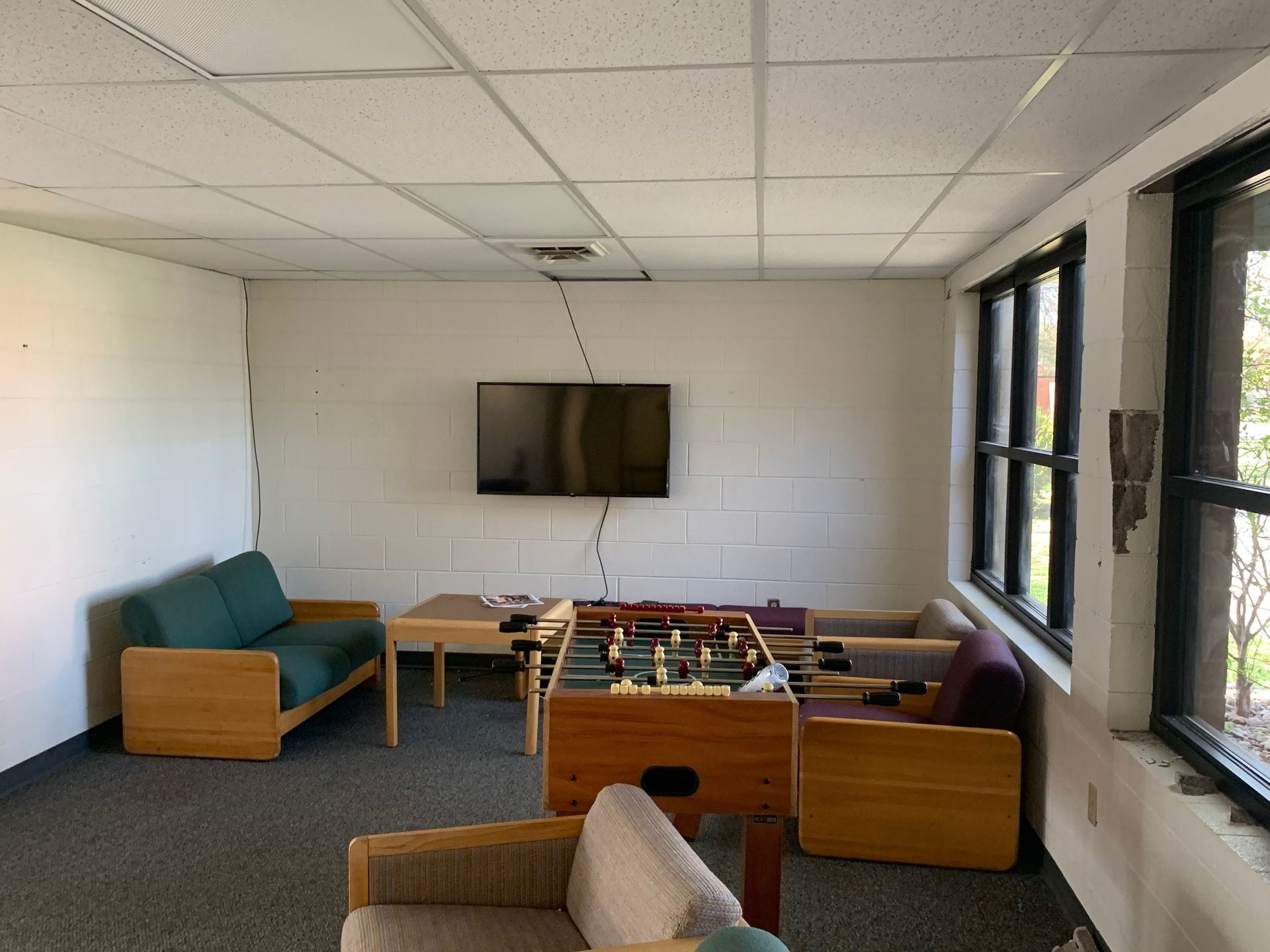 Game room with foosball table, couches, TV on the wall, and windows.