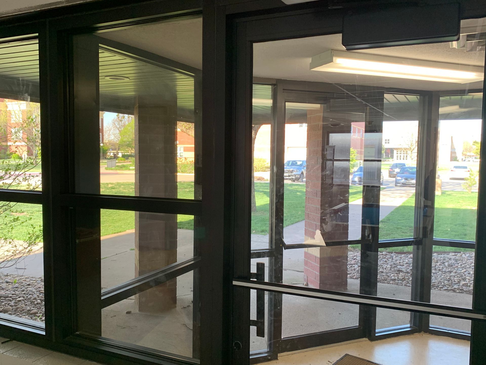 Glass entrance doors and windows; view to exterior; brick pillars and cars visible.