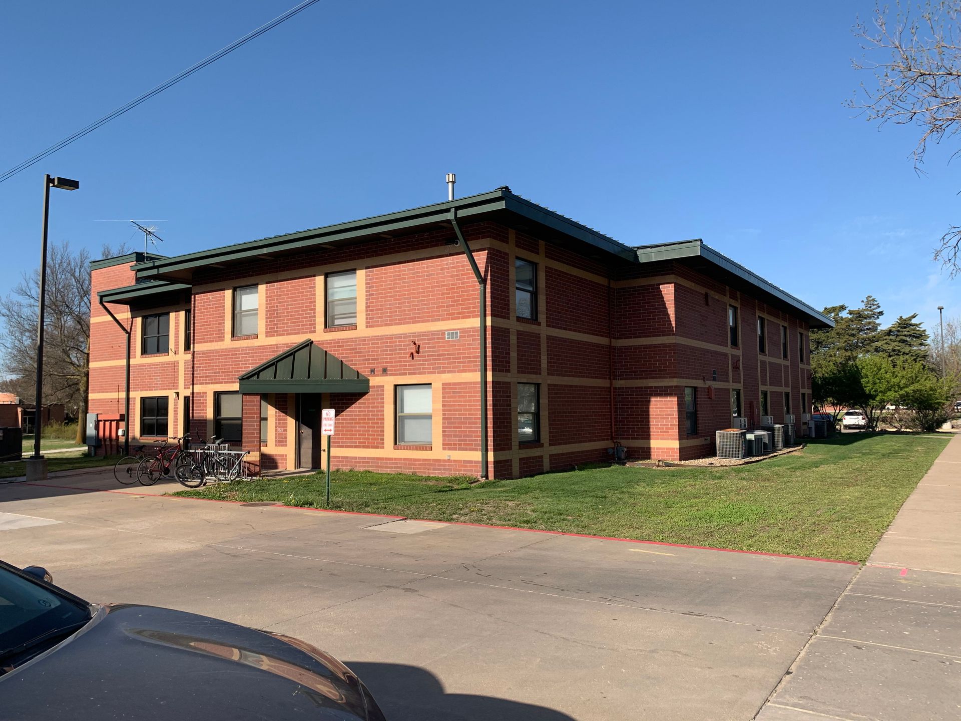 Two-story brick building with green trim, windows, and a small awning; blue sky.