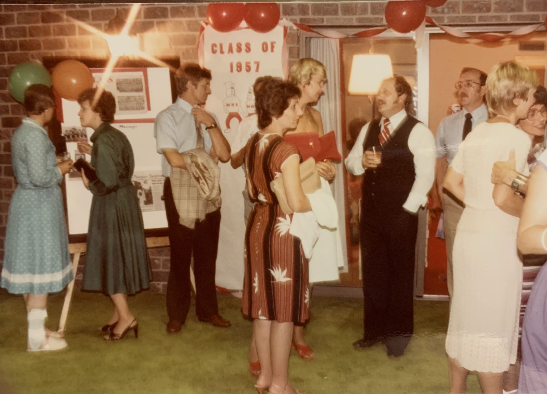 Party with people. Class of 1967 banner, balloons, and retro dresses. A man wears a vest.