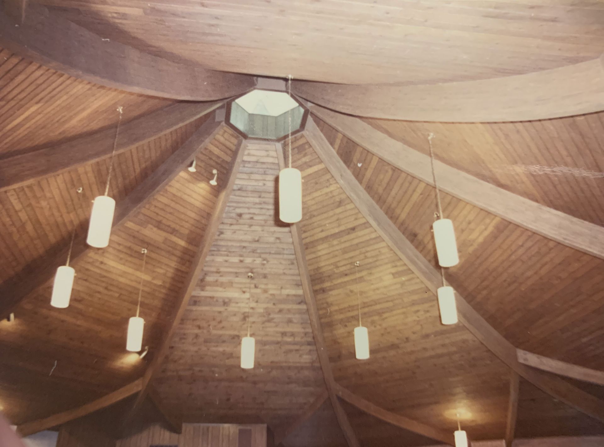 Wooden, circular ceiling with hanging lights and a central skylight.