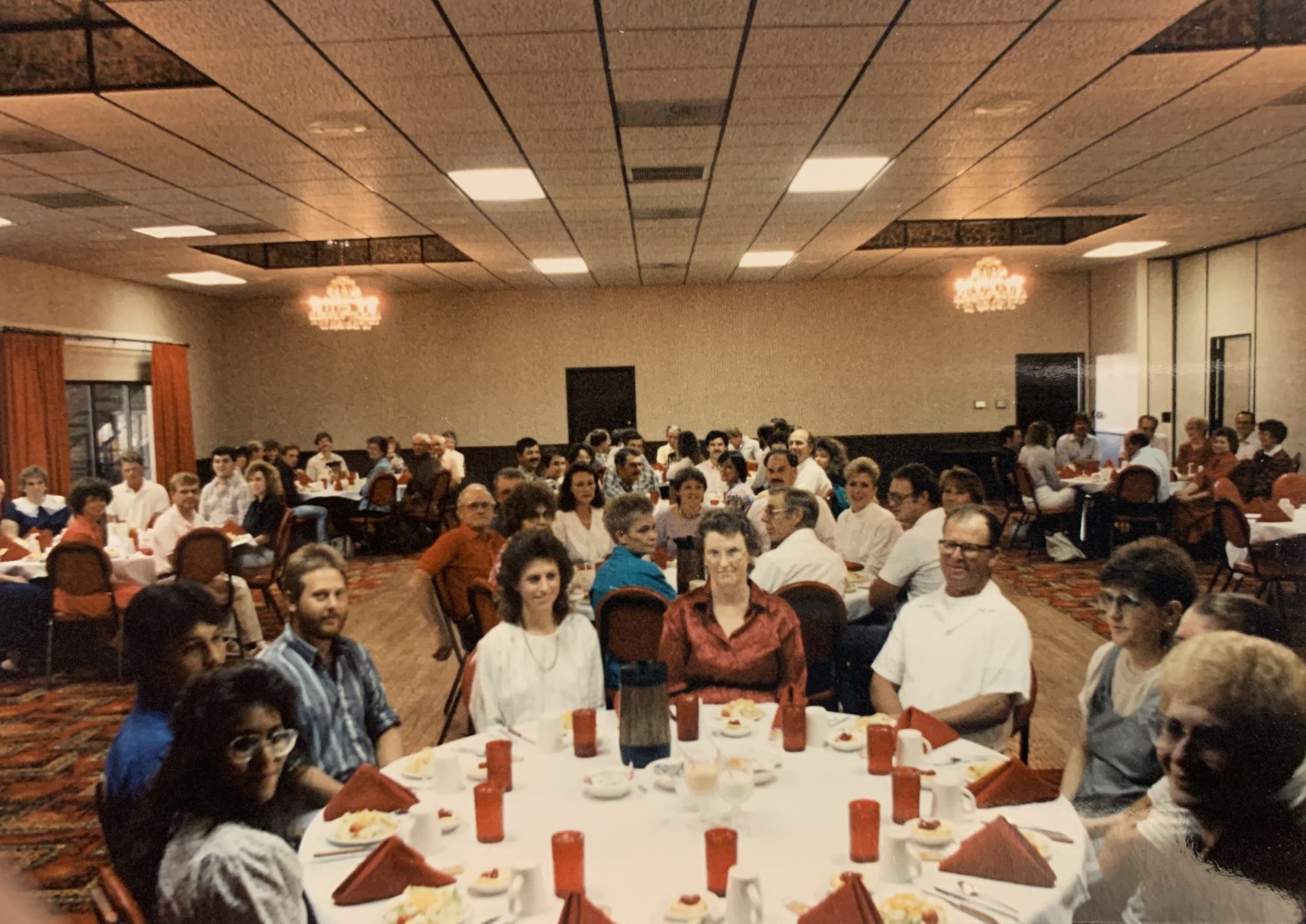 Large banquet hall filled with people seated at round tables. Some are facing the camera.
