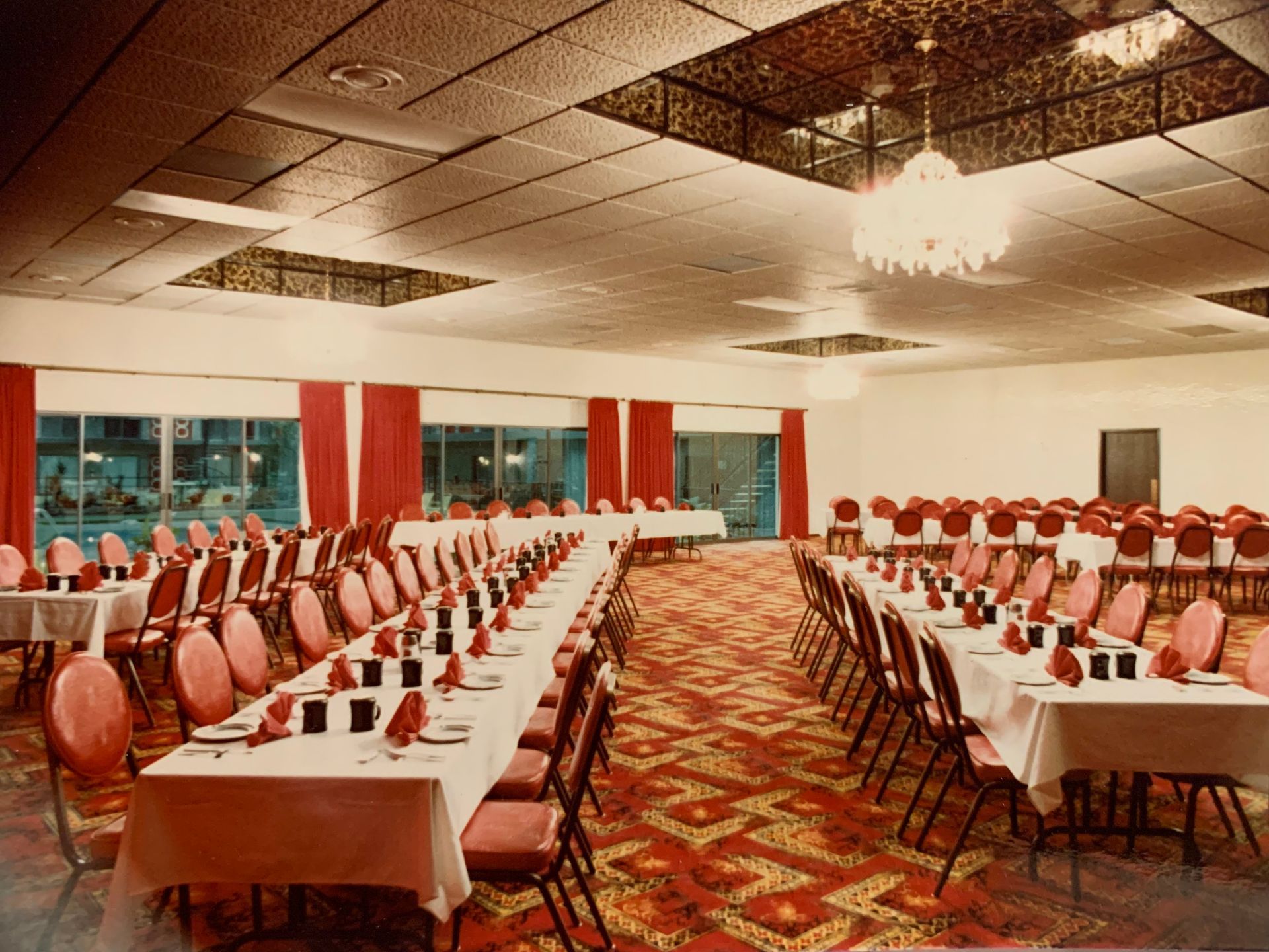 Banquet hall set for a large event, with long tables covered in white linens and red chairs, red carpet.