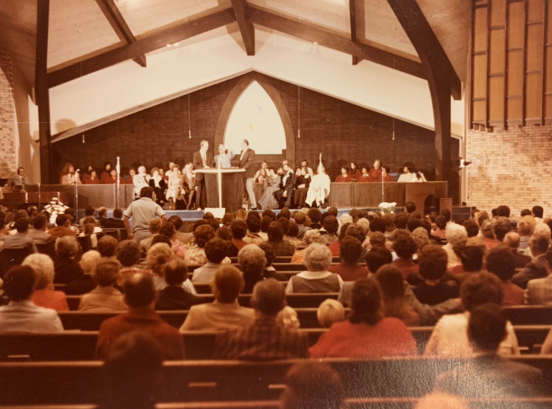 Church service with many people in pews, choir and preacher on the stage.