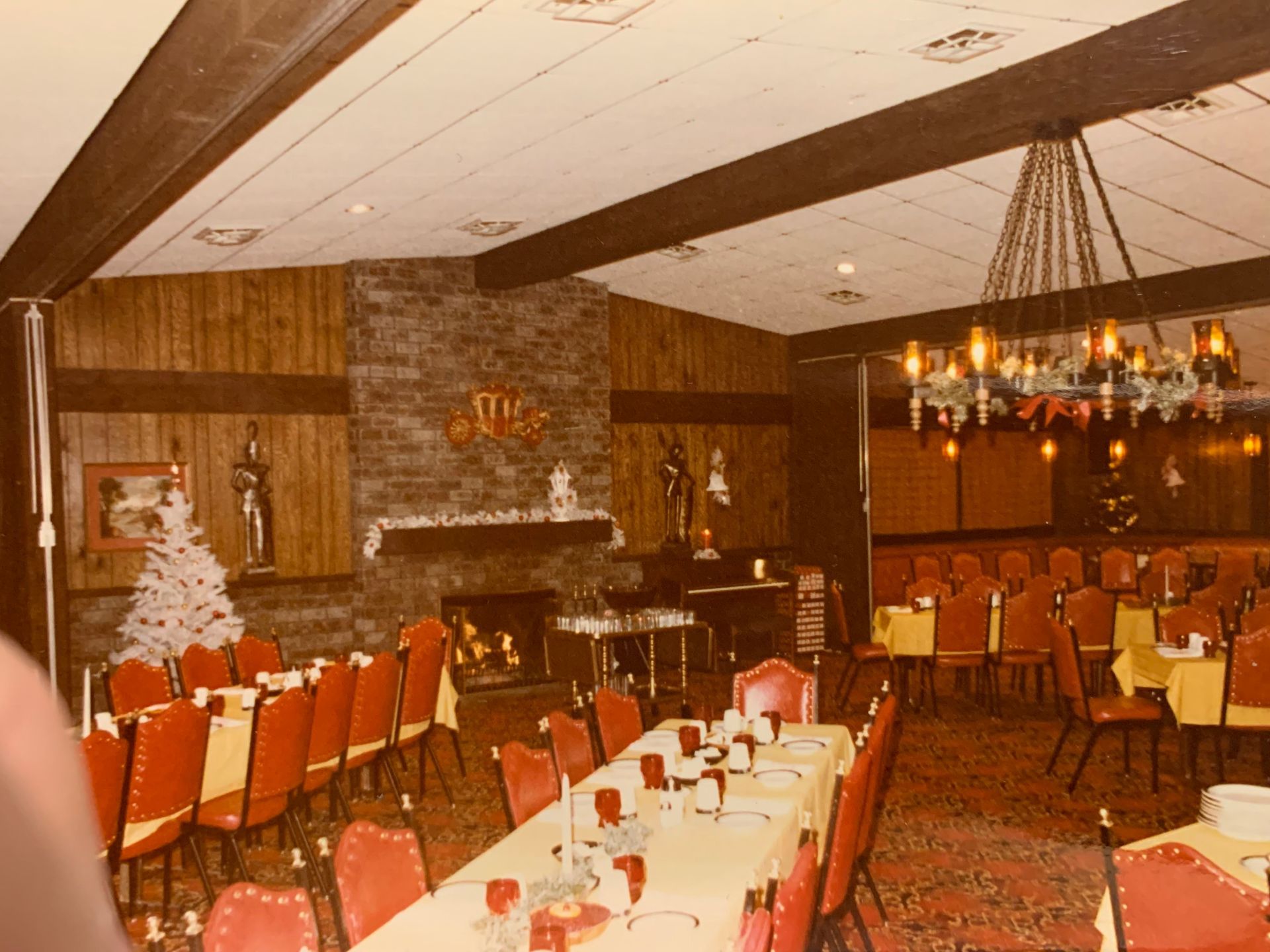 Restaurant interior: Red chairs, yellow tablecloths, fireplace, decorative chandelier, Christmas decorations.