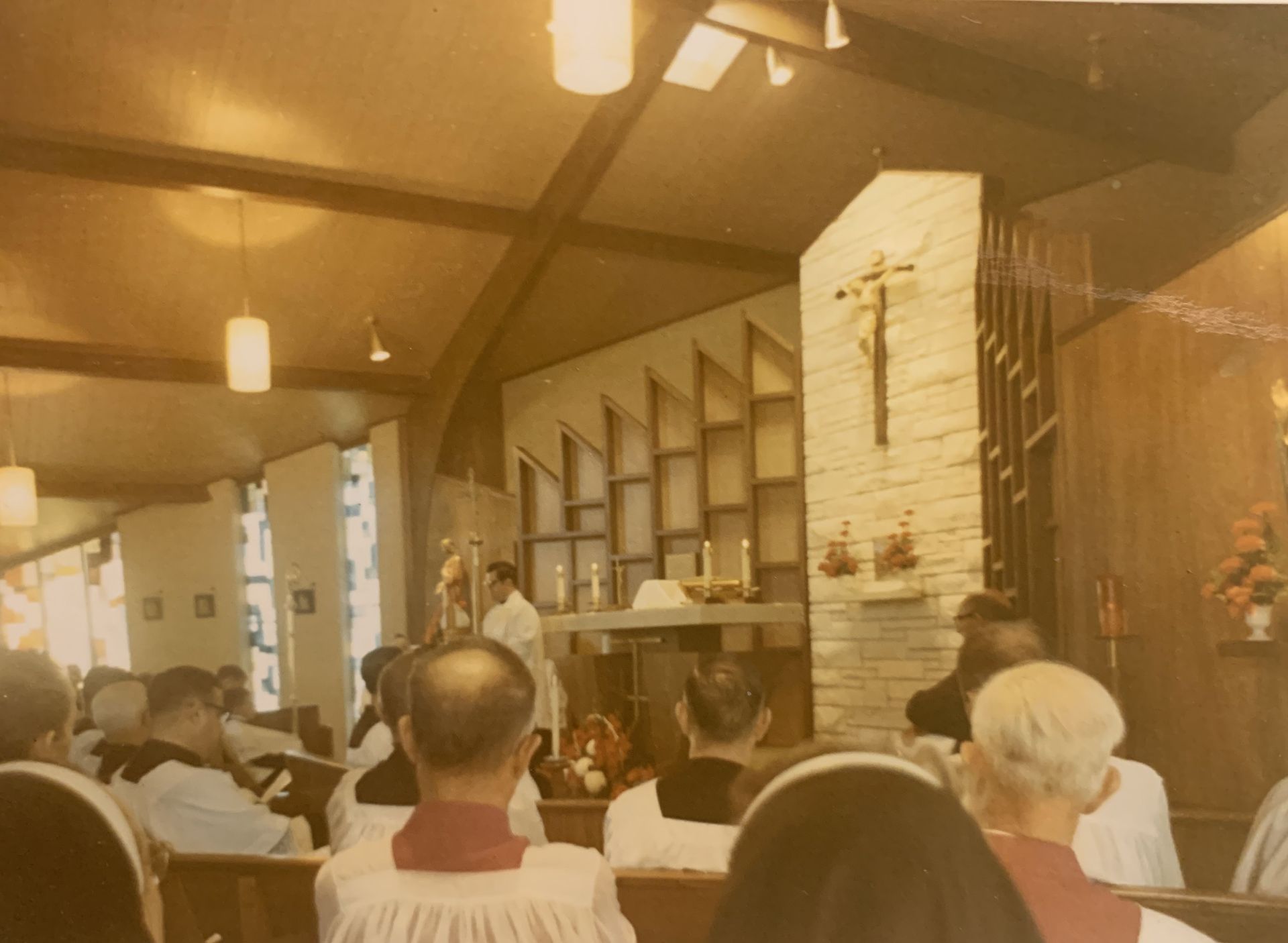 Interior church scene; priest at altar, congregation seated. Wooden paneling, stained glass windows.