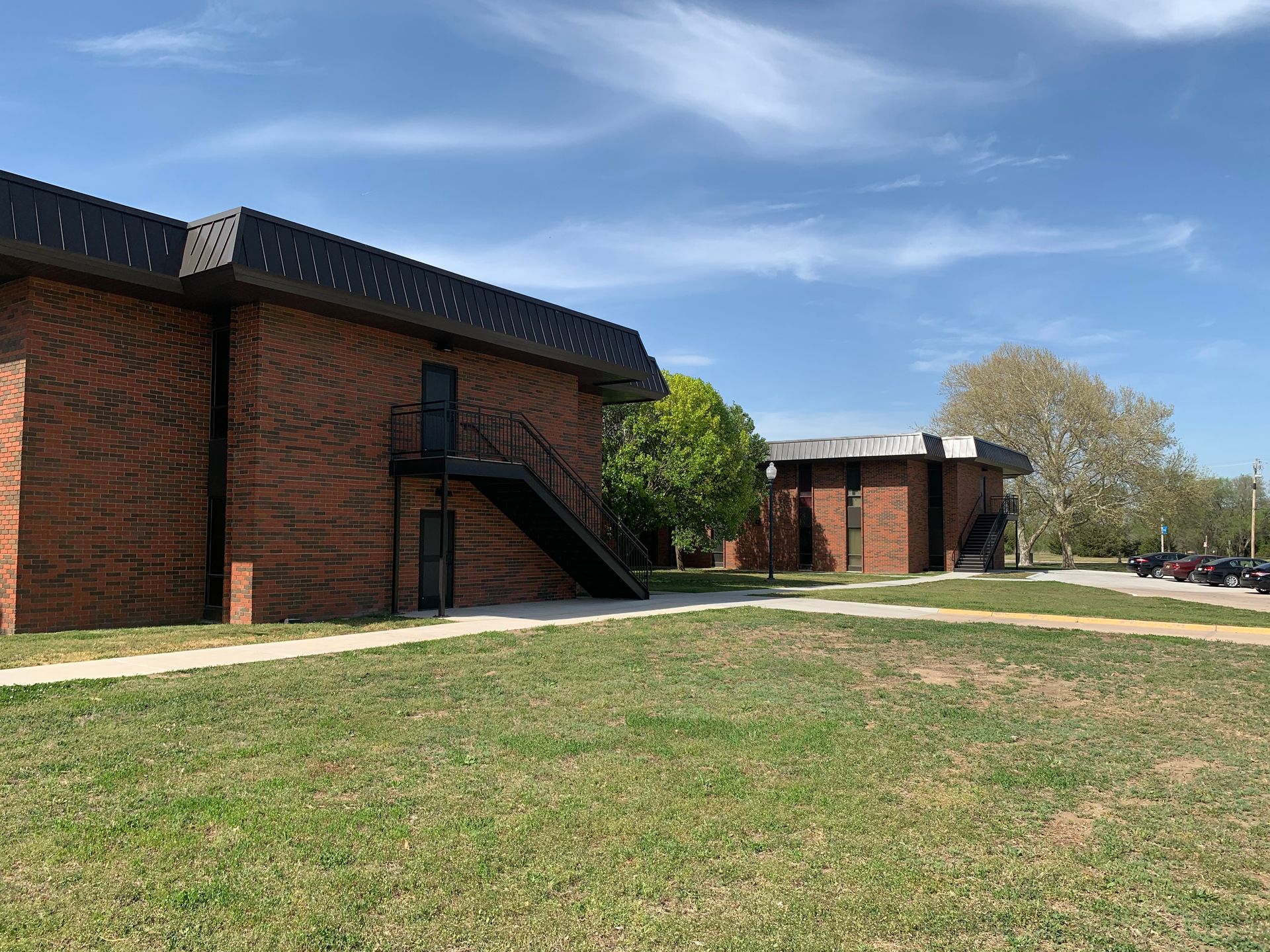Red brick buildings with black trim and a grassy lawn under a blue sky.