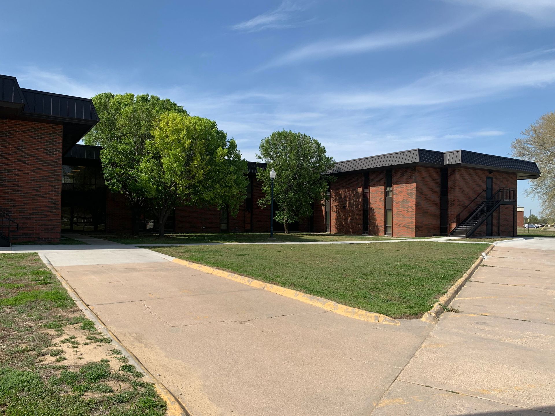 Brick school building with a small grassy area and trees on a sunny day.