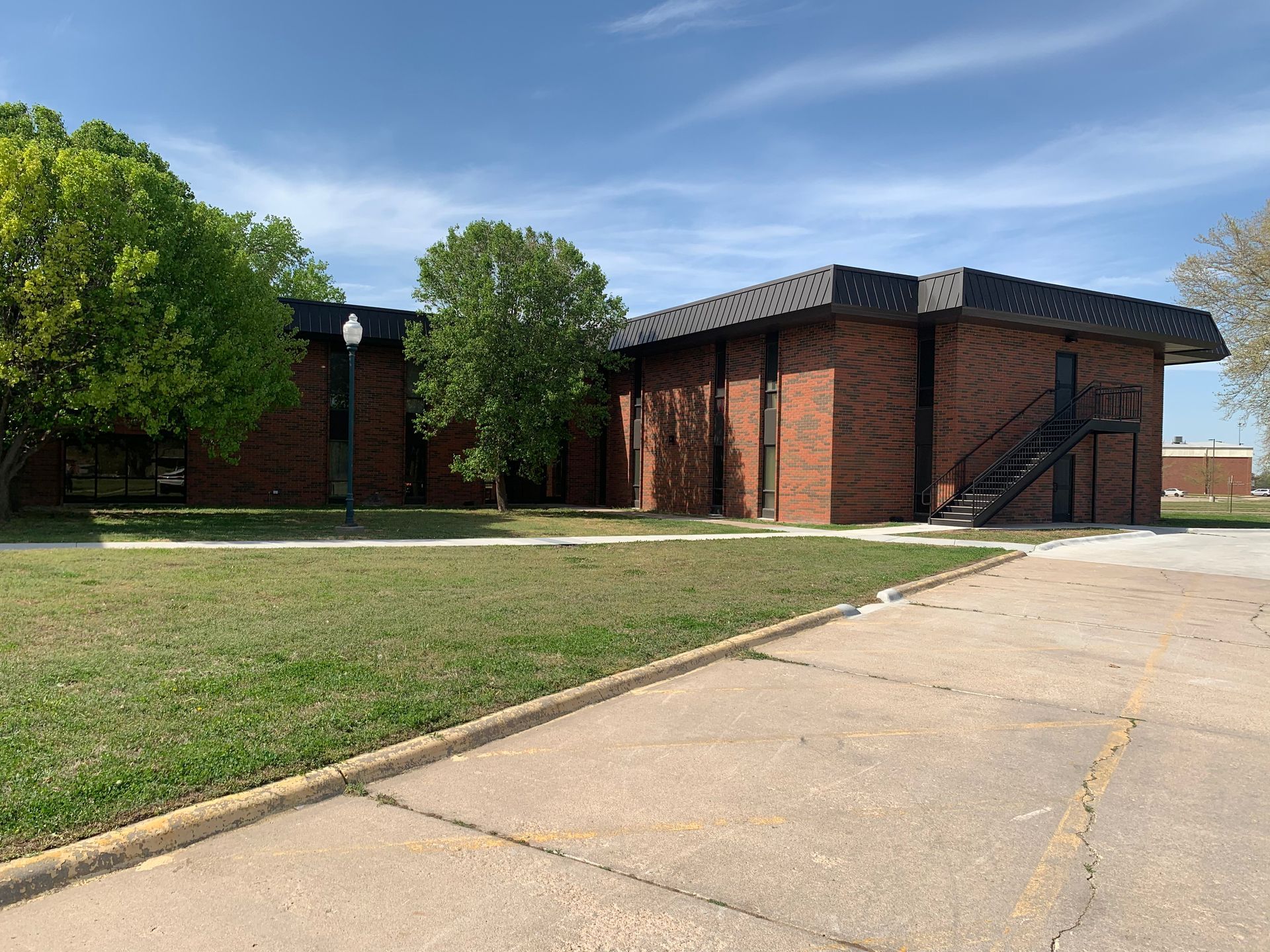 Brick building with black roof; exterior stairs, green lawn, trees, and blue sky.