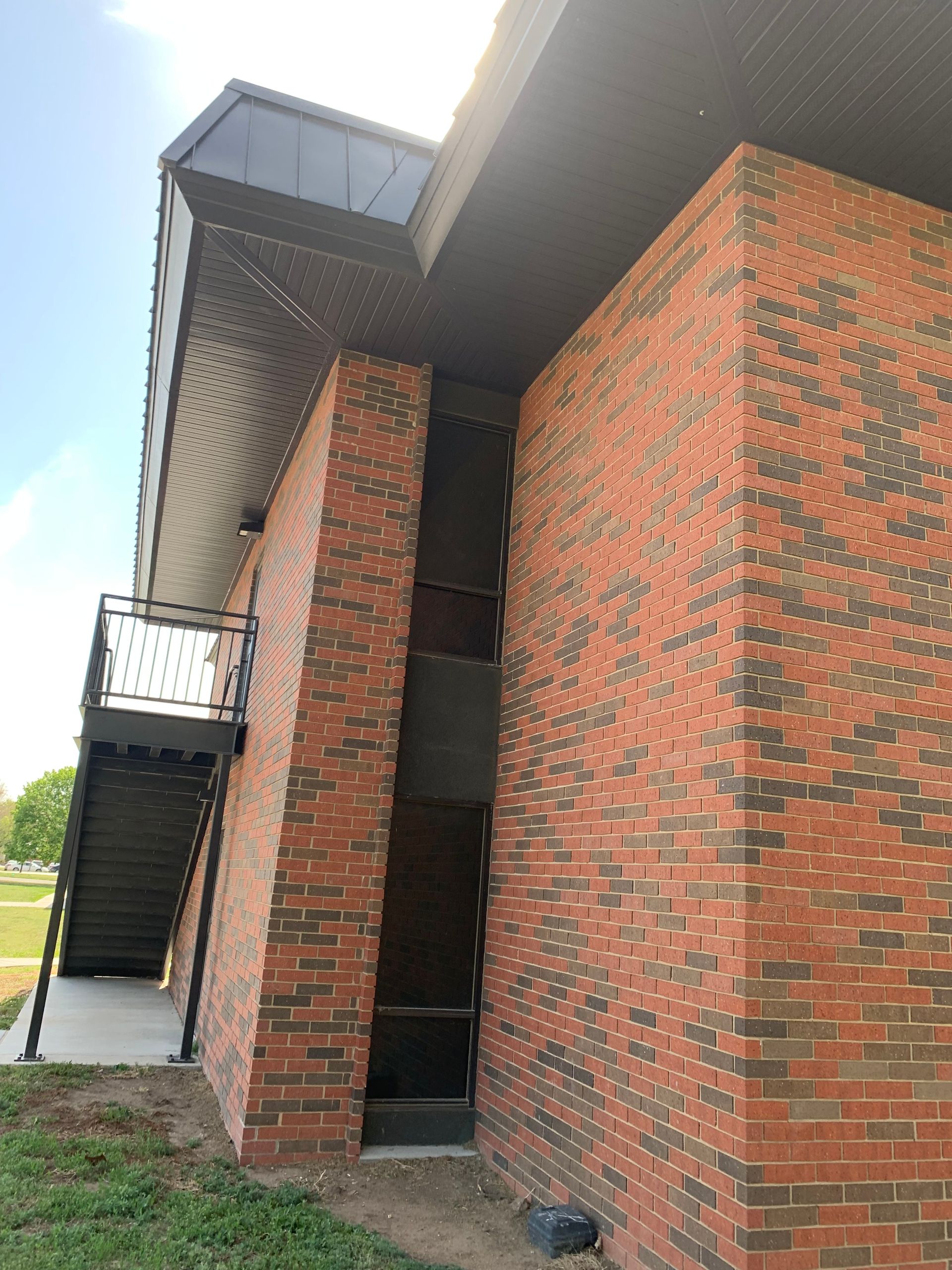 Red brick building with a black metal stairway. Black roof overhangs. Blue sky in the background.