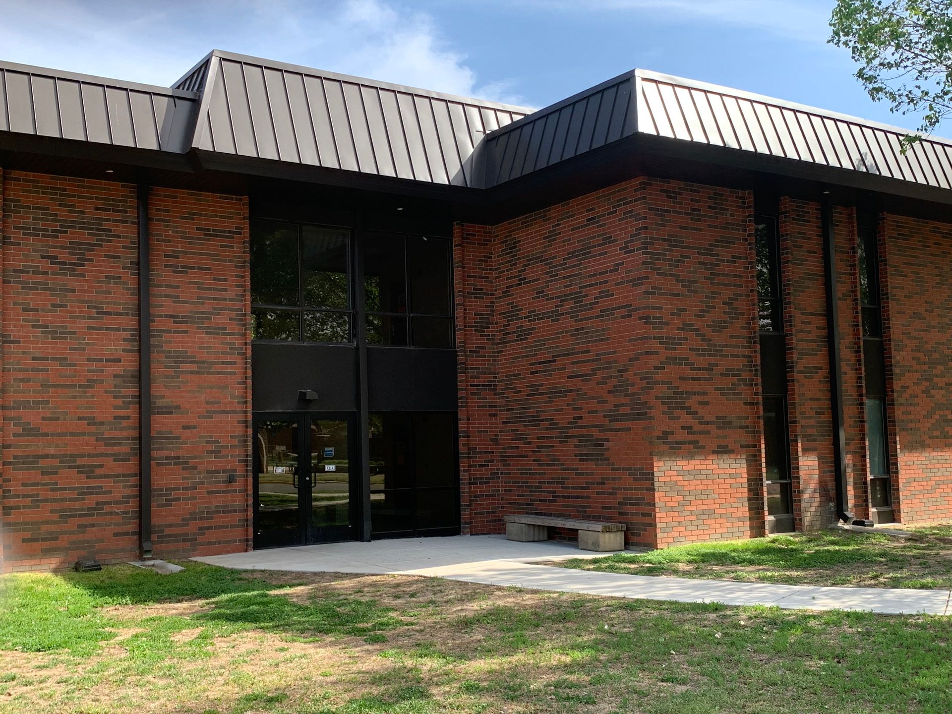 Brick building with black trim and windows, a dark metal roof, and a concrete path.