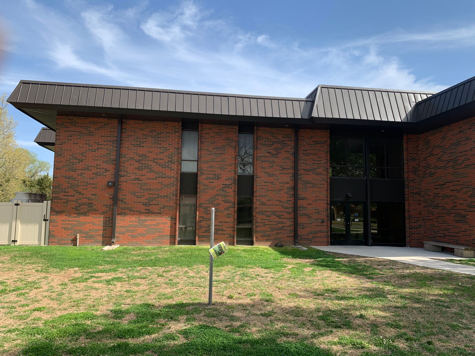 Red brick building with dark roof and windows, set on a lawn under a blue sky.