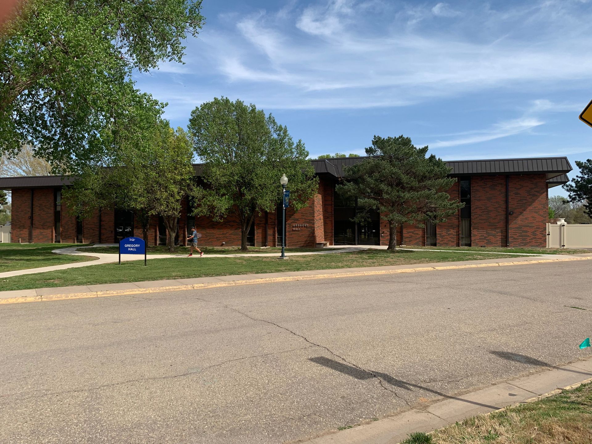 Brick building with trees, blue sign, and a road under a blue sky.