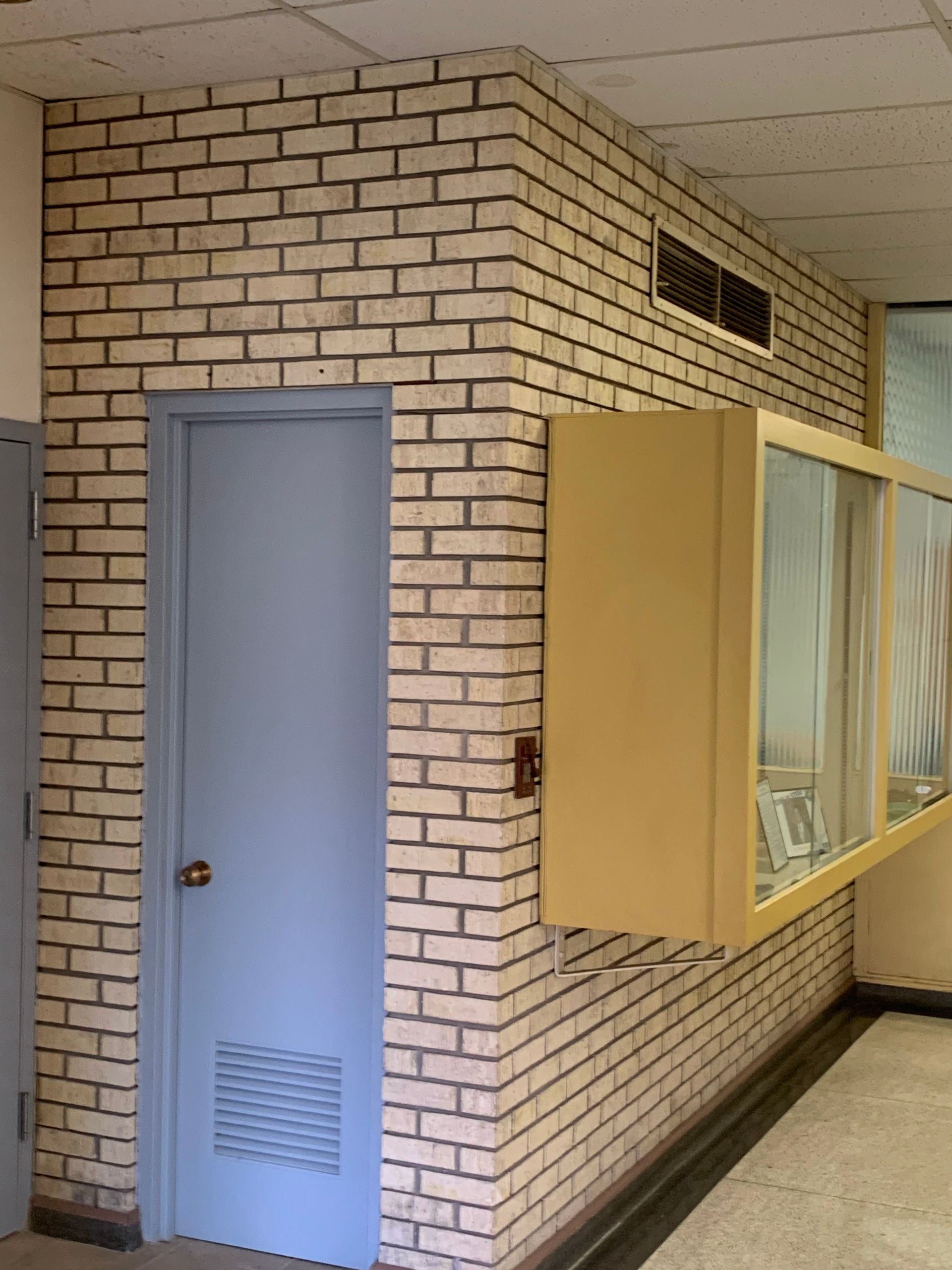 Blue door and yellow-framed display case in a brick-walled hallway.