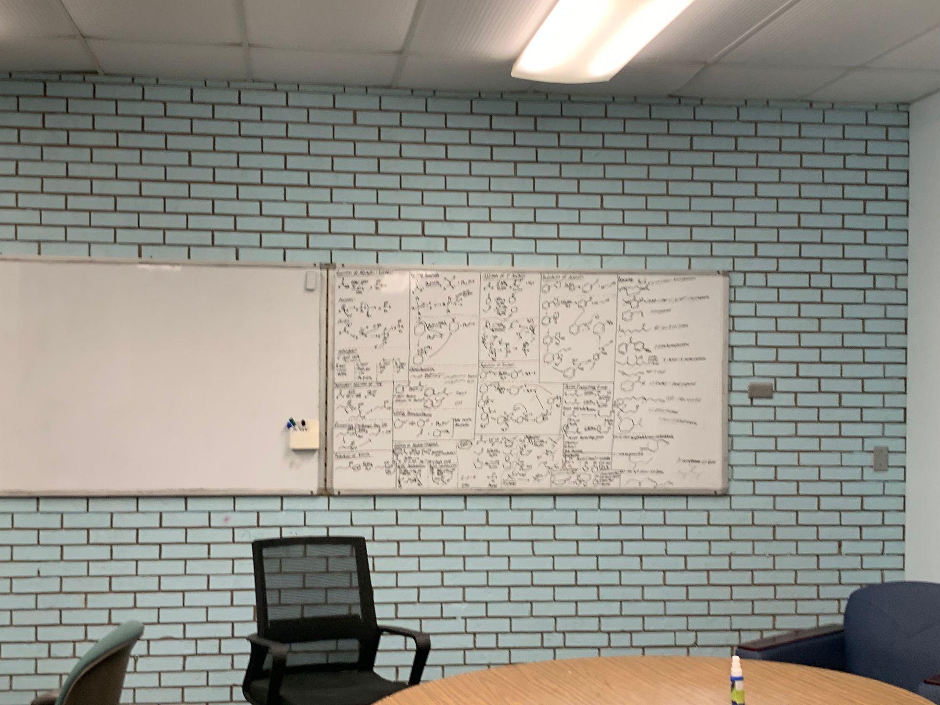 Whiteboards on a light blue brick wall, a black chair, and a round table in a classroom.