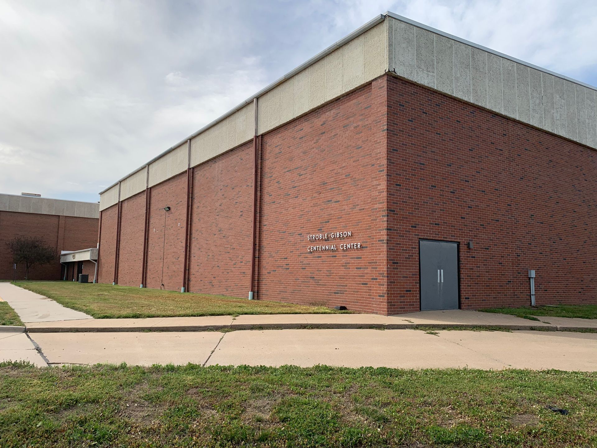 Red brick building with a white upper section and a gray door. Green grass and sidewalk in front.