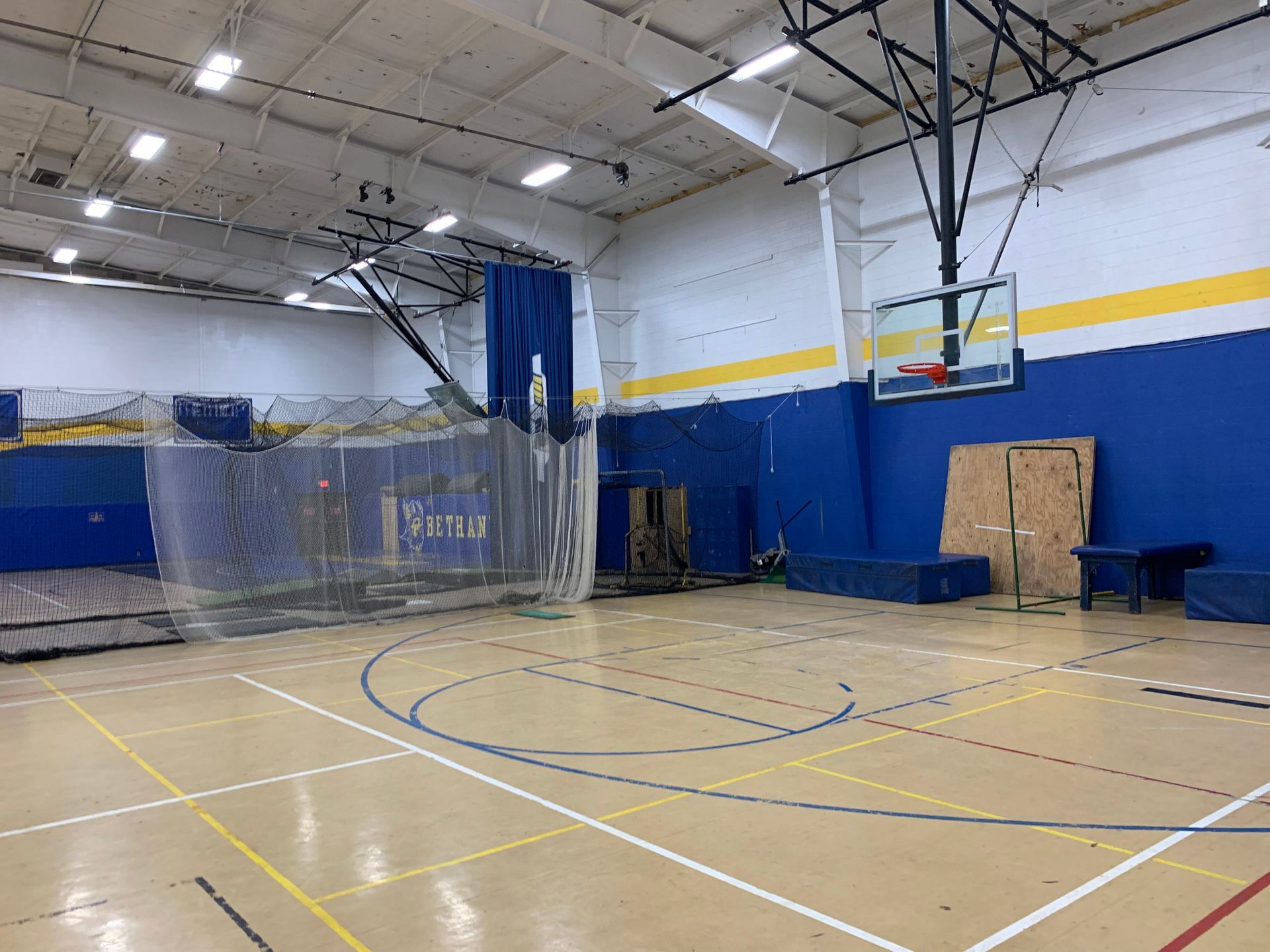 Basketball court with net enclosure, hoop, and blue and yellow walls.