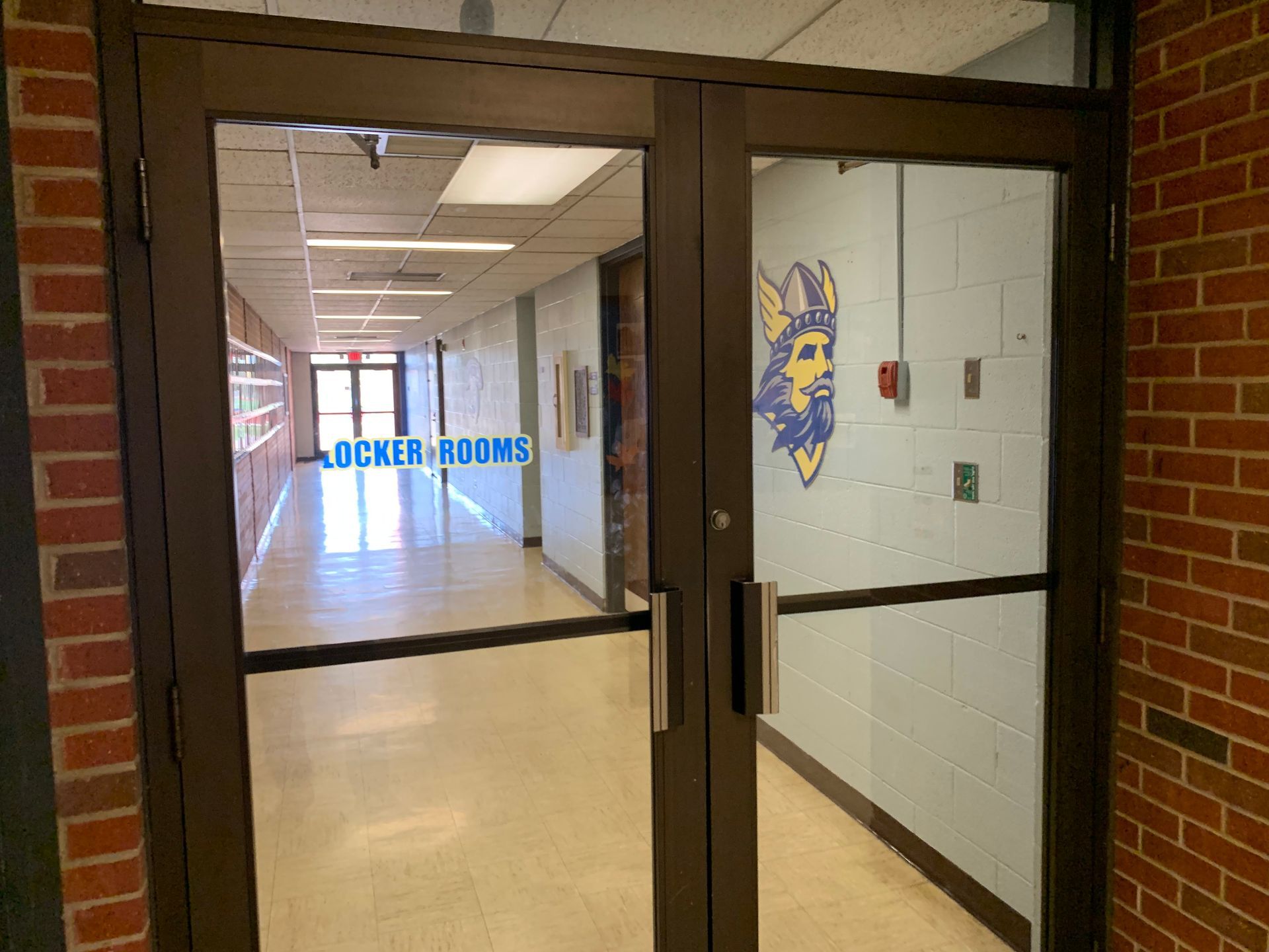 Double doors open to a school hallway, brick walls, a Viking logo.