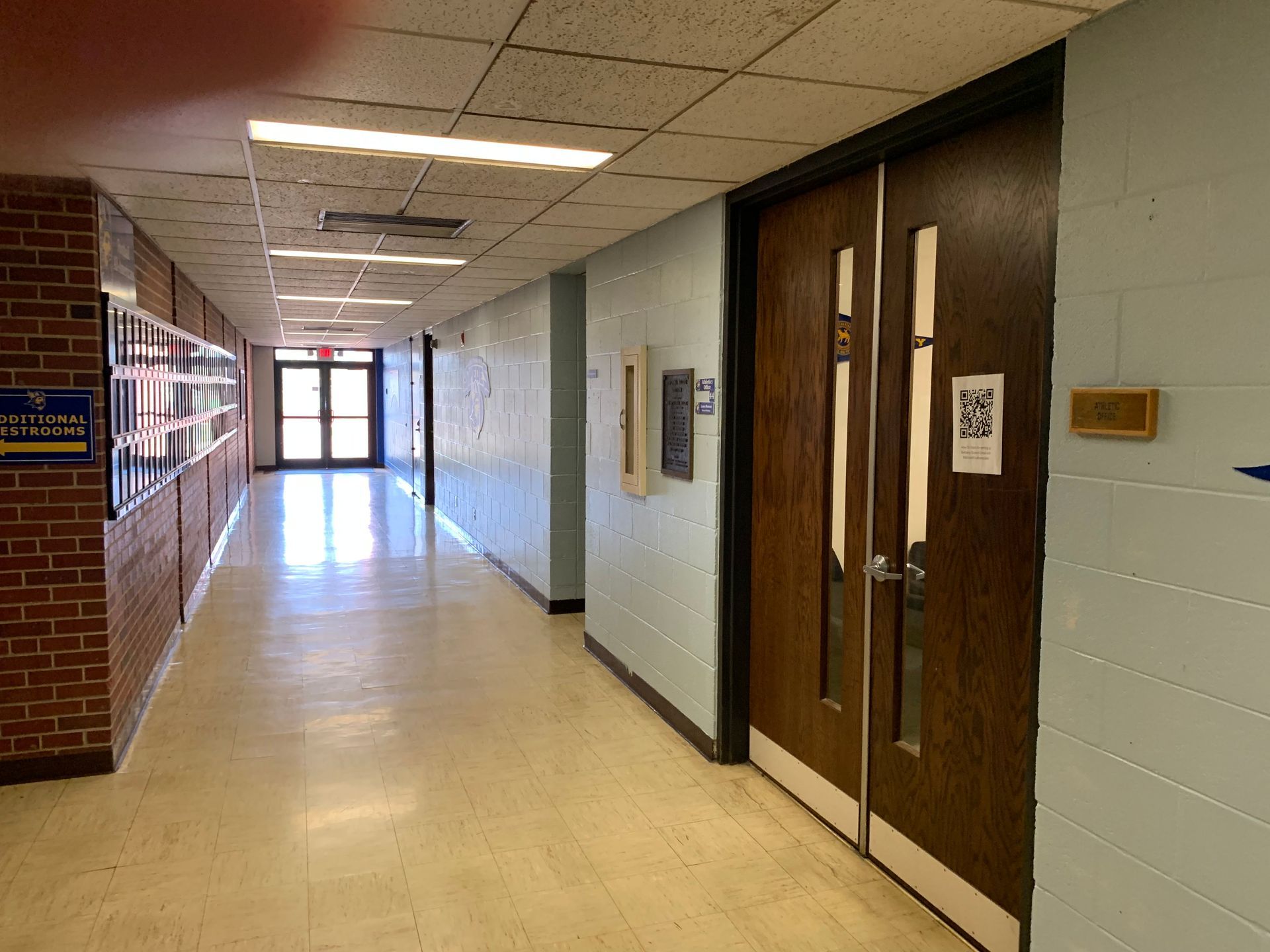 Hallway with brick wall on left, closed double doors on right, and an open door at the end.