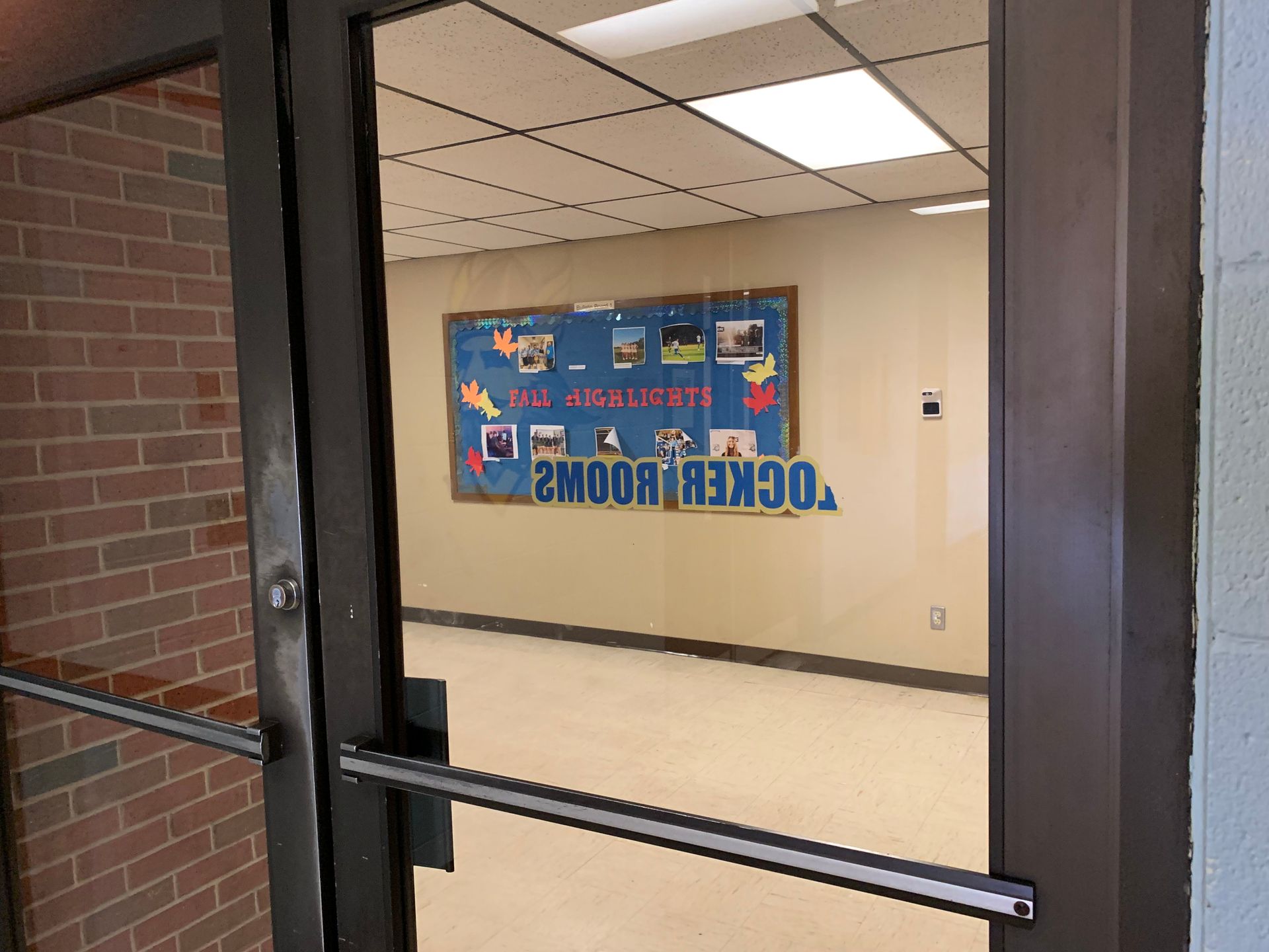 Glass door open to a hallway with a bulletin board that says “locker rooms”.