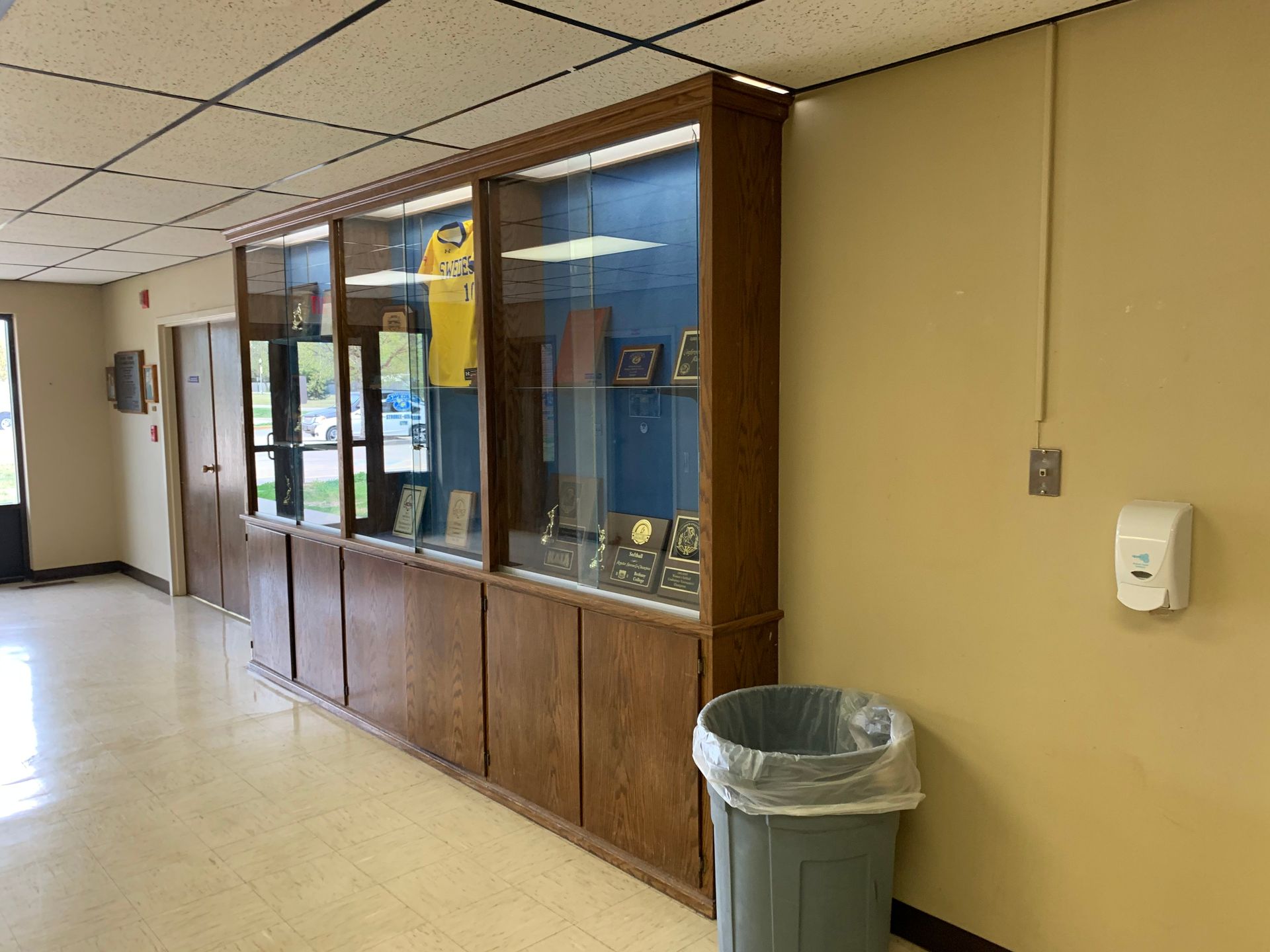 Hallway with wooden display case containing trophies and a jersey, ne