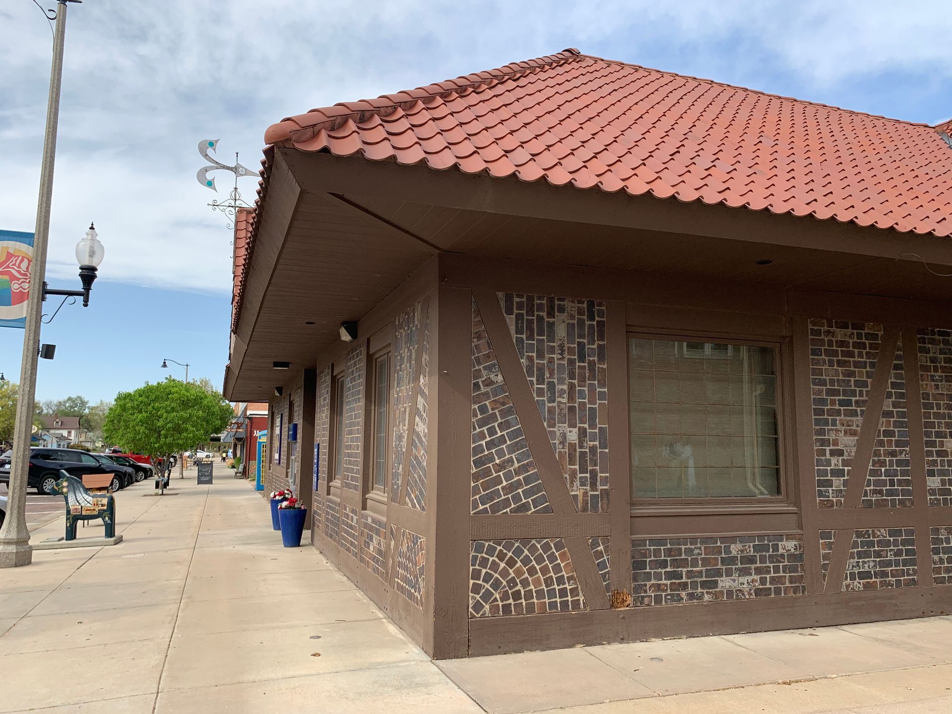 Building with brown trim and red tile roof, on a sidewalk, partially obscured by the street.