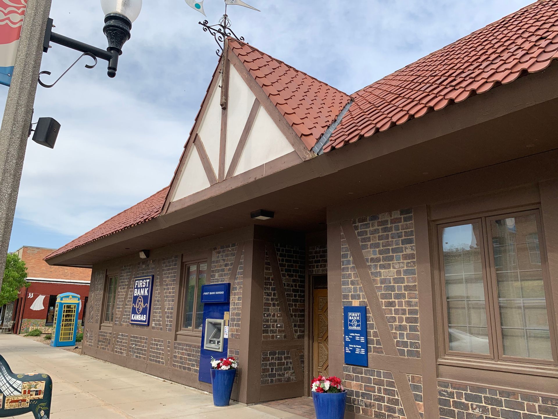 Brown building with a red tile roof and half-timbered style exterior. An ATM and blue signage are visible.