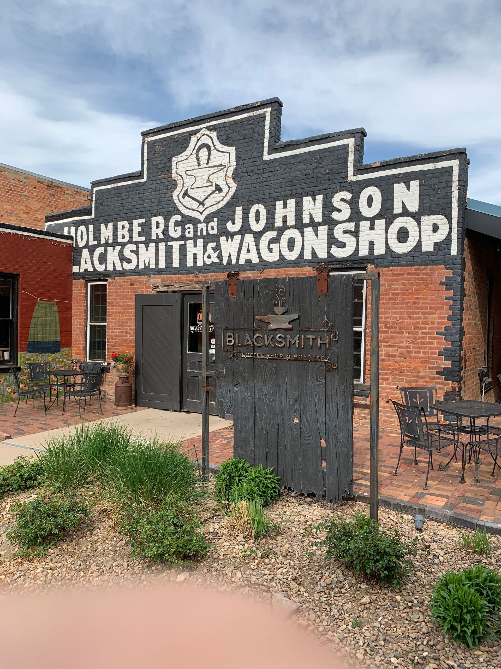 Holmberg and Johnson Blacksmith & Wagon Shop building with sign, doorway, brick facade.
