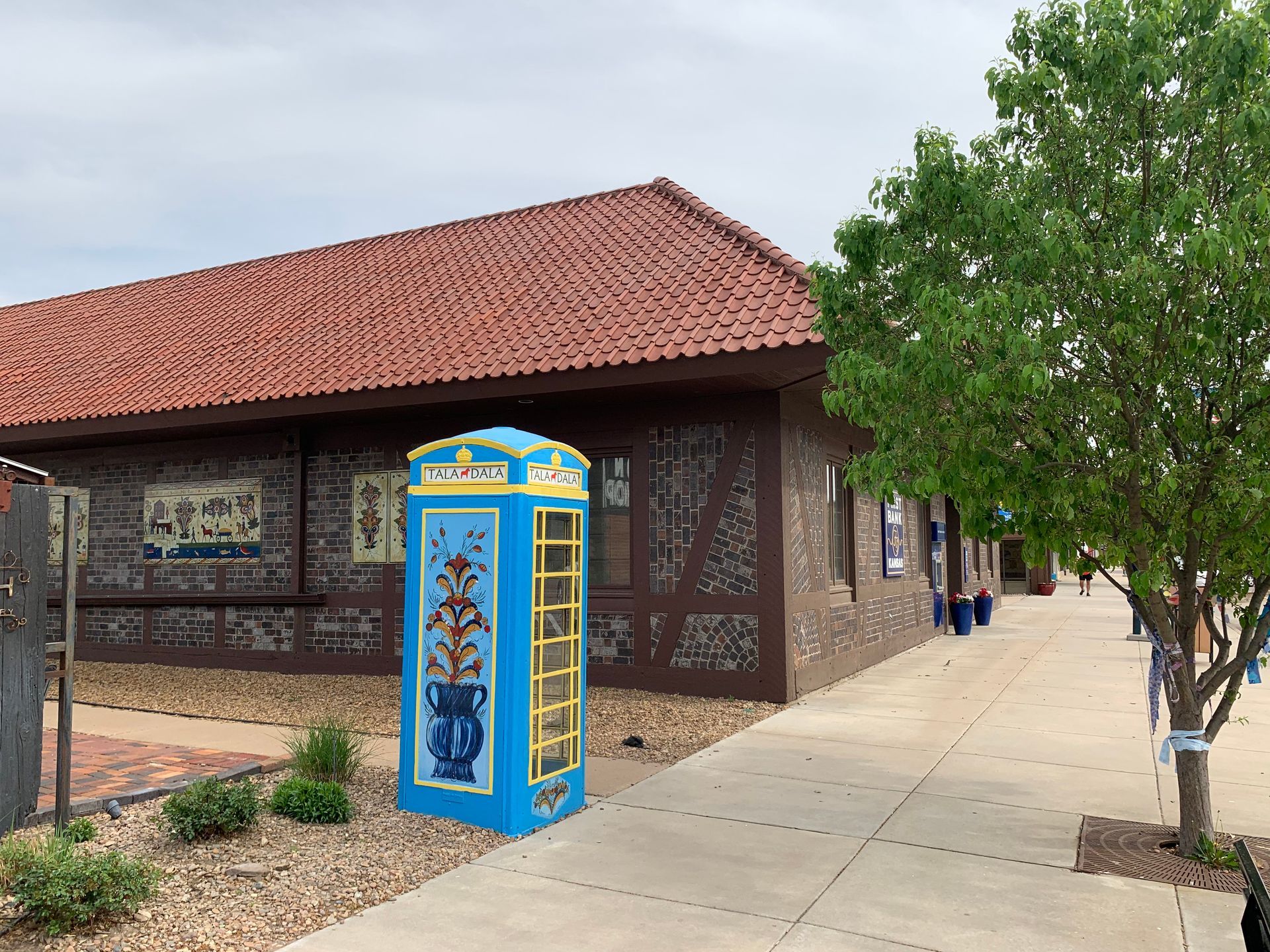 A turquoise phone booth decorated with floral designs sits outside a brown building with a red-tiled roof.