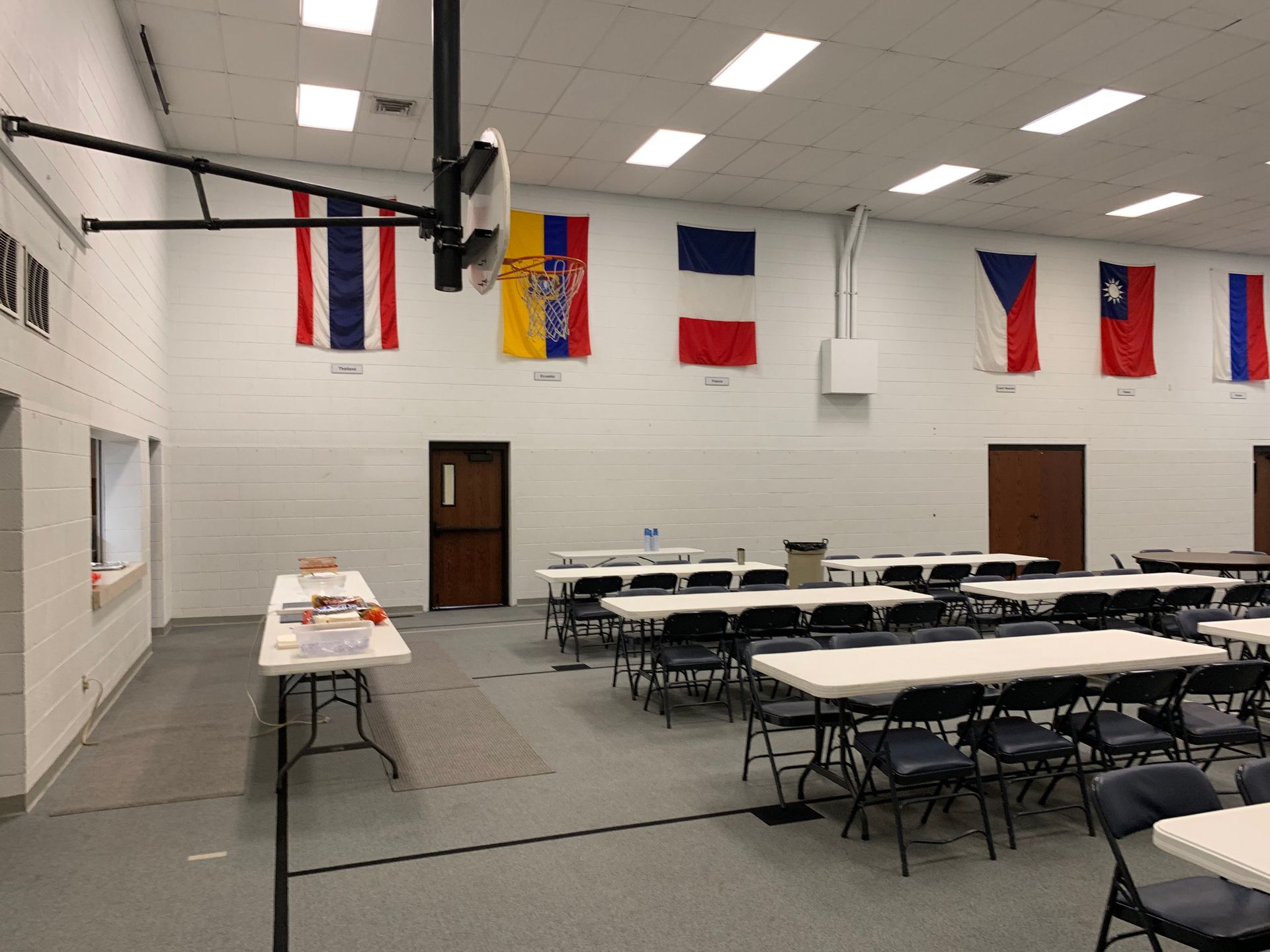Large room with white tables and chairs, flags hanging on wall.