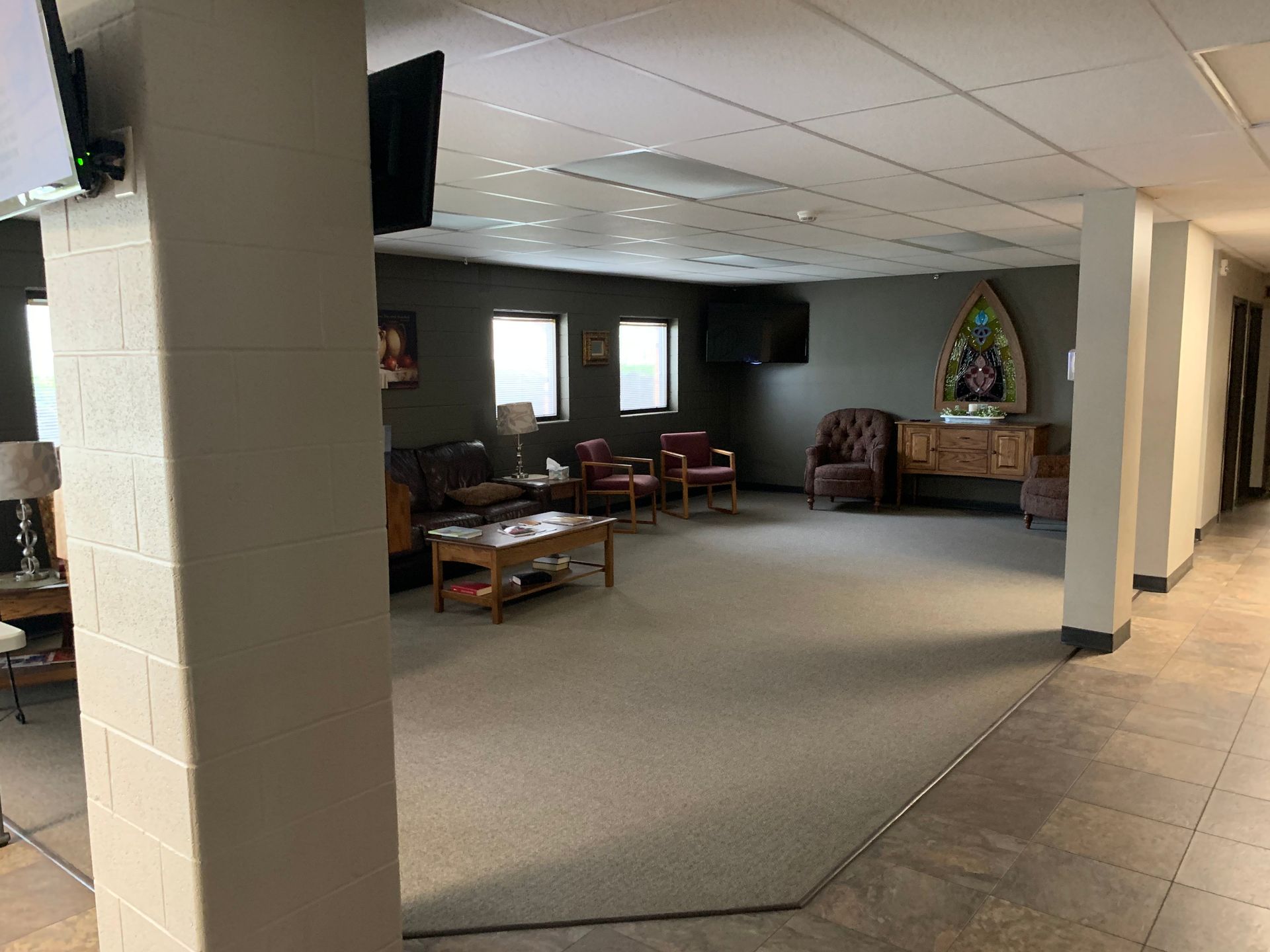 Waiting room with couches, chairs, and a table, in a building with a light gray carpet.