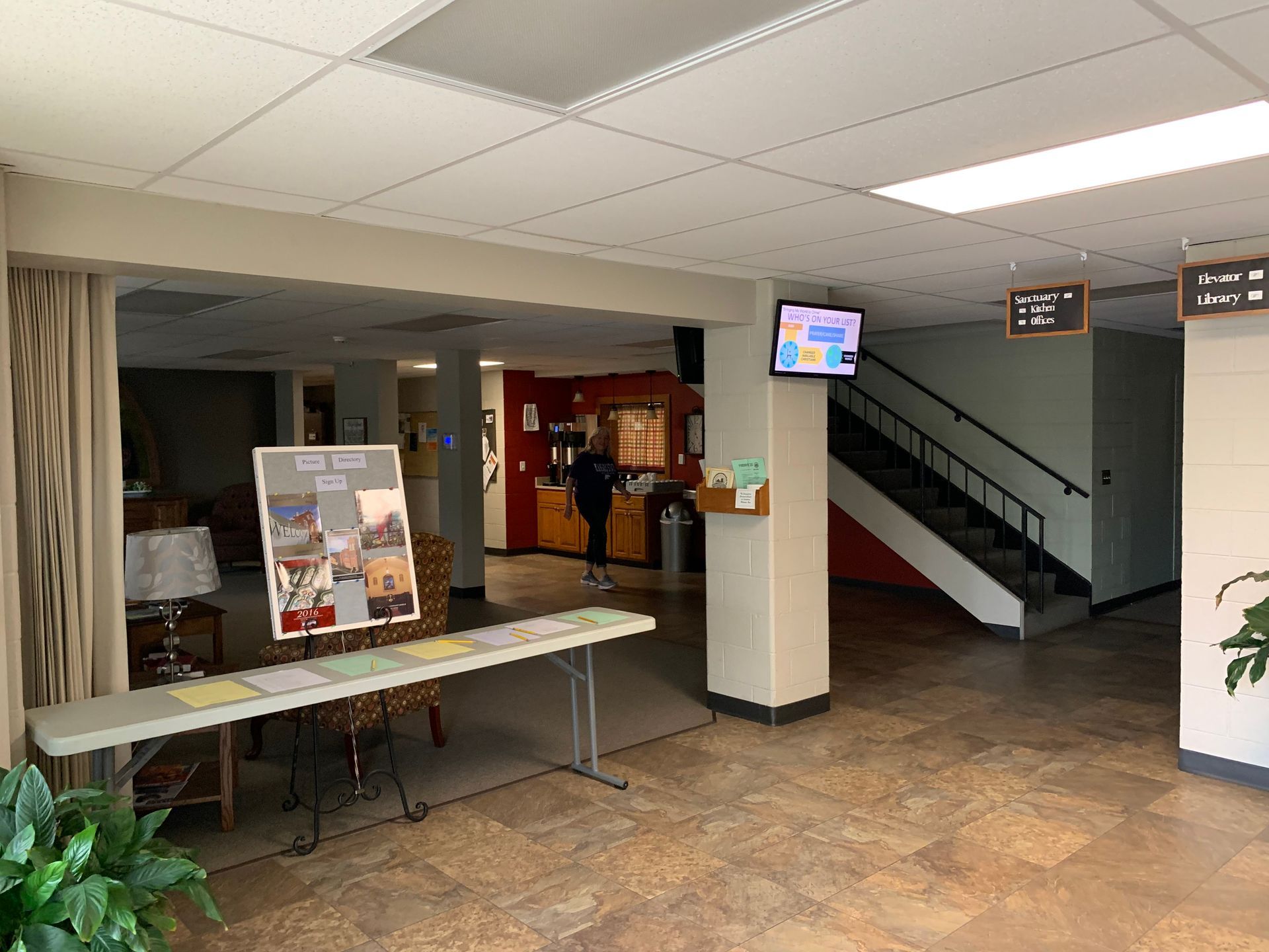 Lobby with informational displays, staircase, and a person near a reception desk.