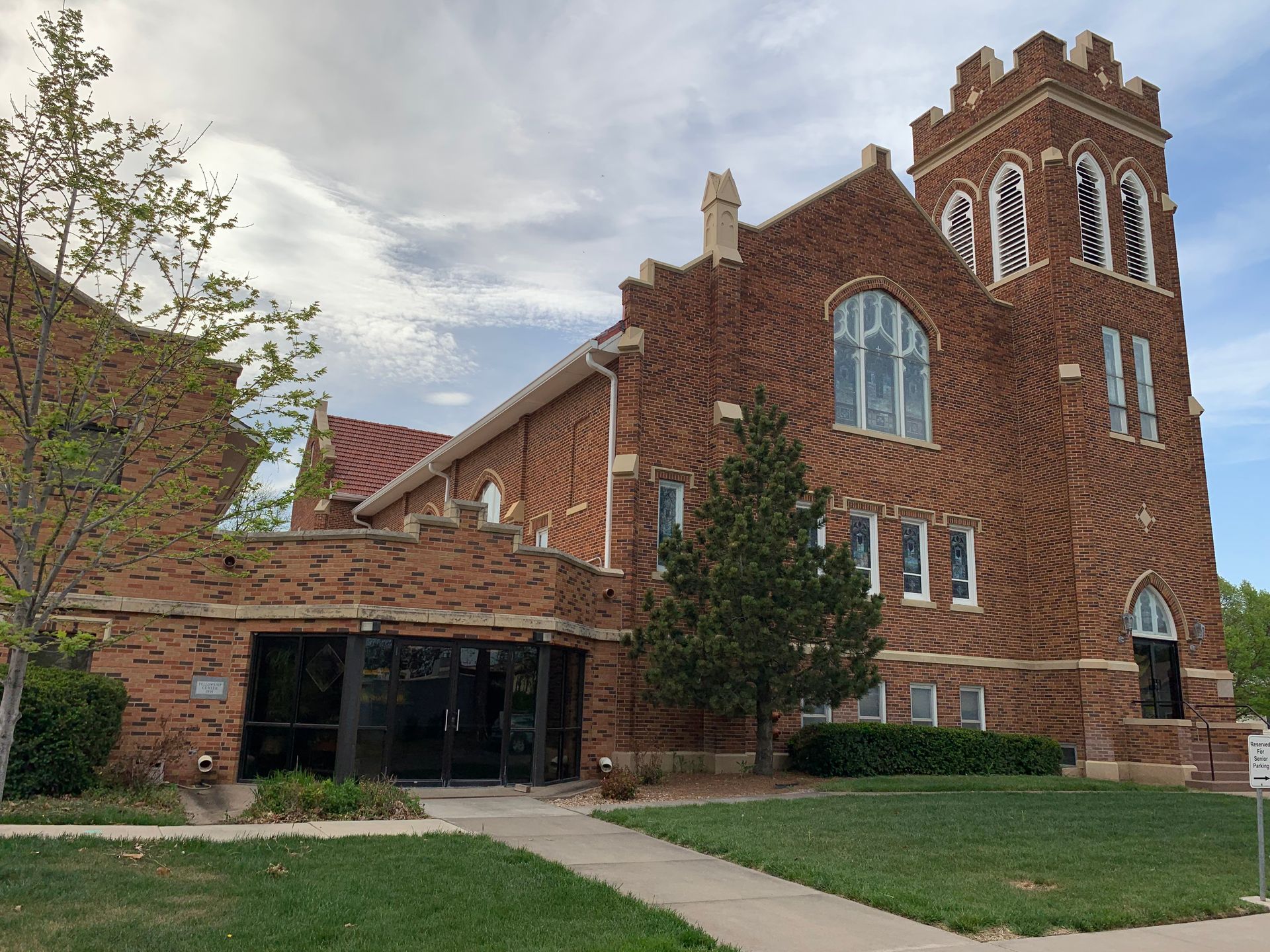 Brick church building with a tower, green grass, and a cloudy sky.