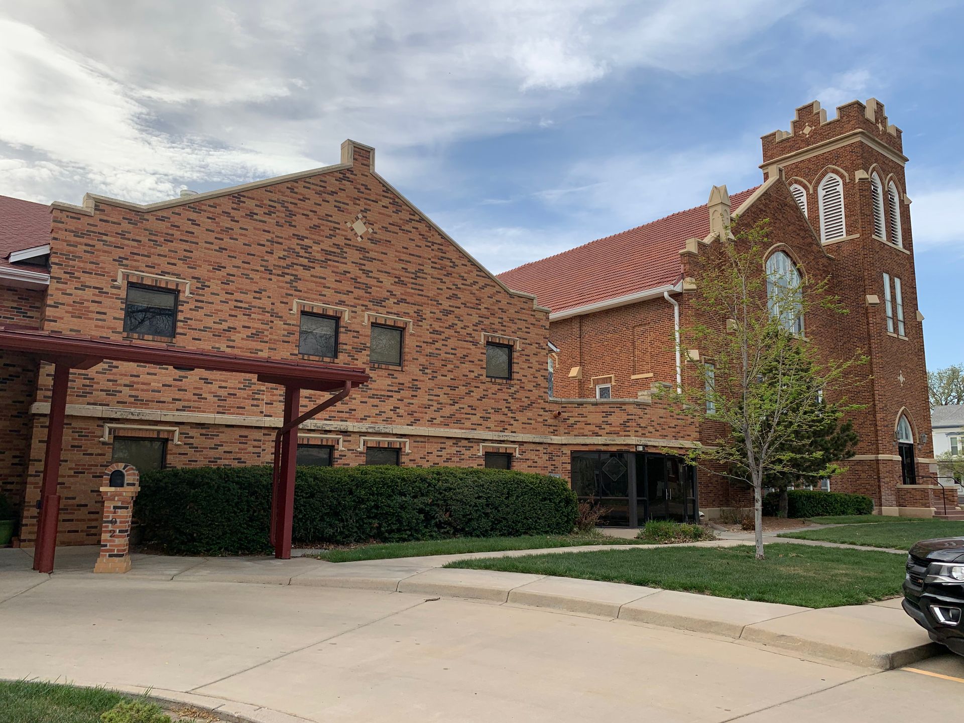 Brick church building with a tower, red roof, and green lawn on a cloudy day.